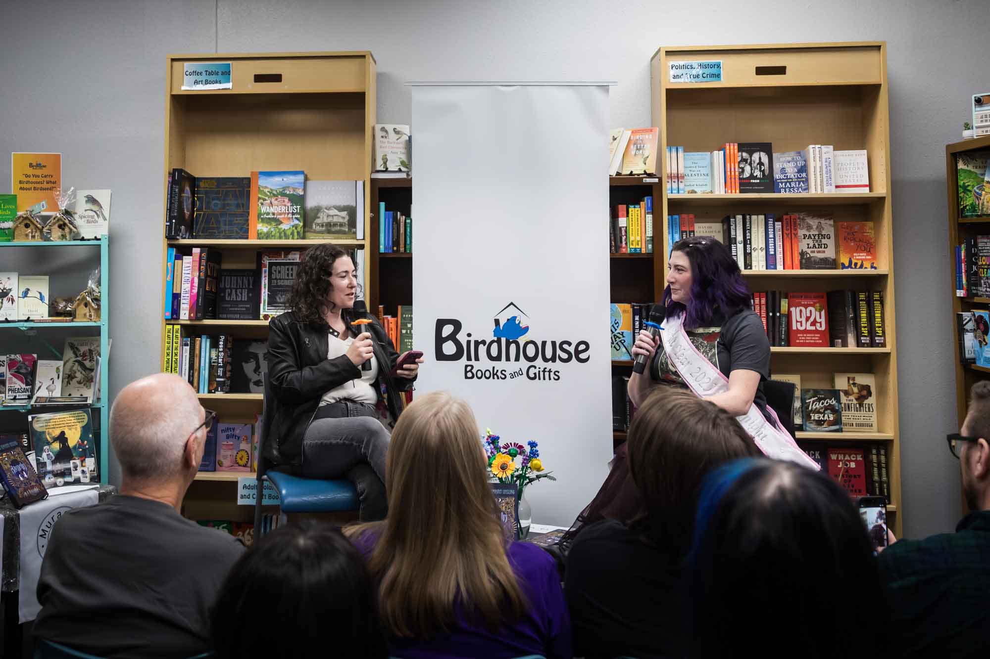 Austin book launch party photos of authors Nancy Knight and Erin Cotter speaking into microphone in front of shelves filled with books