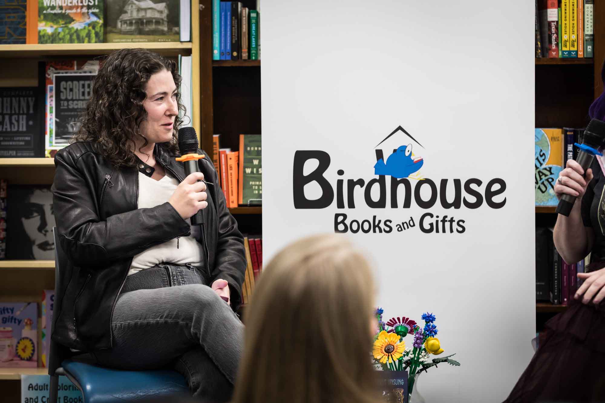 Austin book launch party photos of author Erin Cotter speaking into microphone in front of shelves filled with books