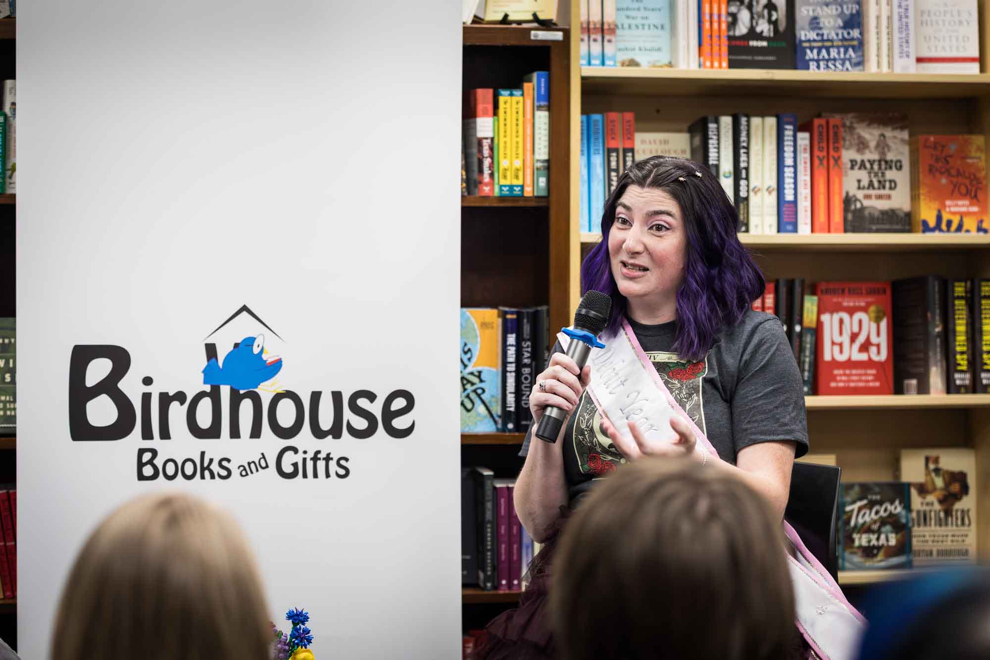 Austin book launch party photos of author Nancy Knight speaking into microphone in front of shelves filled with books