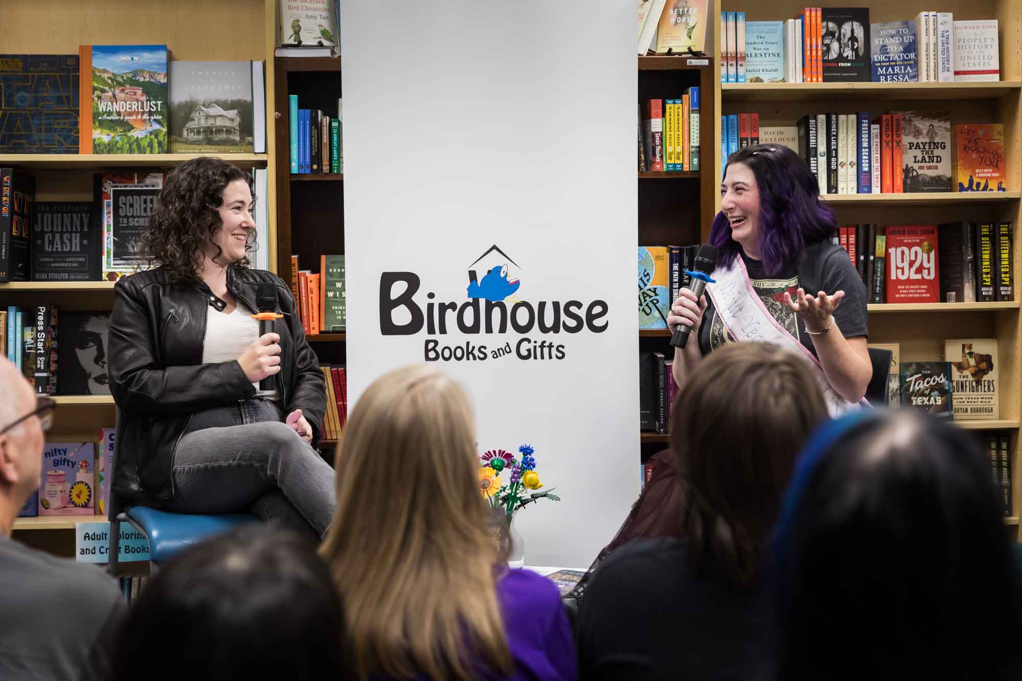 Austin book launch party photos of authors Nancy Knight and Erin Cotter speaking into microphone in front of shelves filled with books