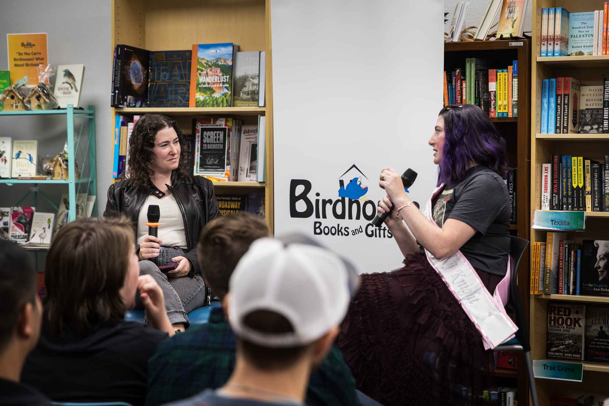 Austin book launch party photos of authors Nancy Knight and Erin Cotter speaking into microphone in front of shelves filled with books