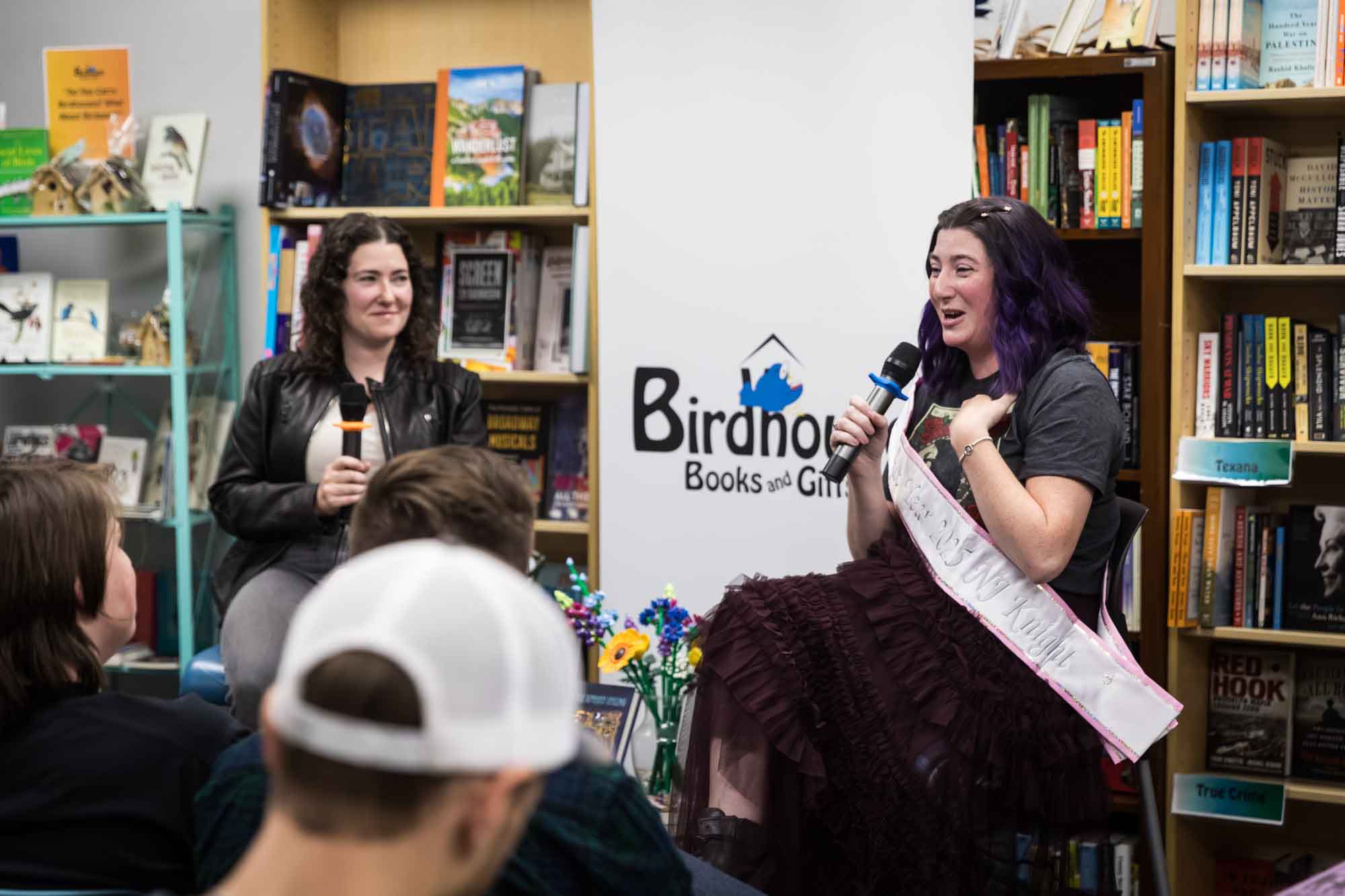 Austin book launch party photos of authors Nancy Knight and Erin Cotter speaking into microphone in front of shelves filled with books