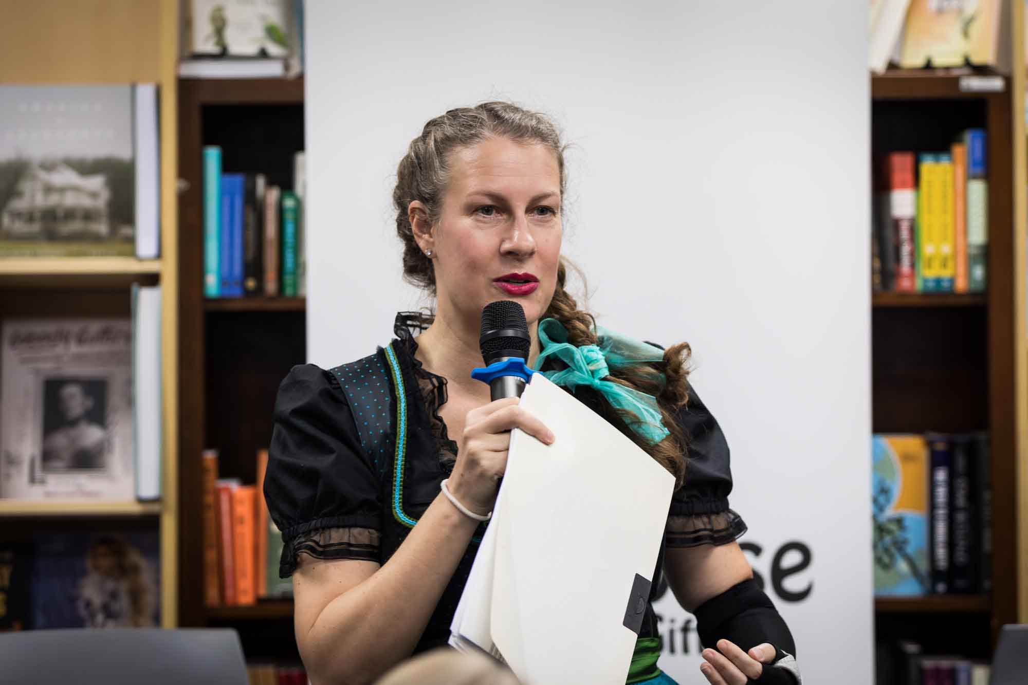Austin book launch party photos of publisher Britta Jensen speaking into microphone while holding paper