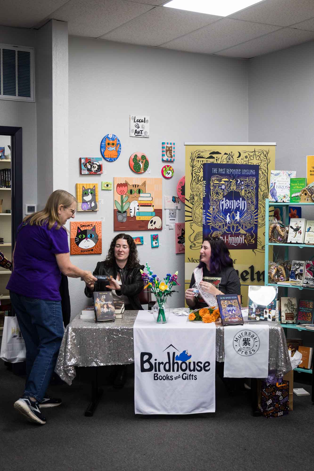 Austin book launch party photos of authors Erin Cotter and Nancy Knight seated at table chatting with woman wearing purple shirt