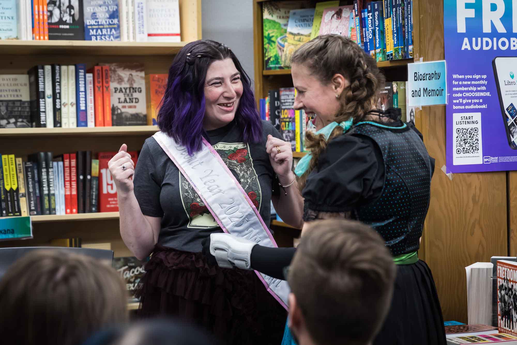 Austin book launch party photos of publisher Britta Jensen presenting pink sash to author Nancy Knight in front of bookshelf at Birdhouse Books