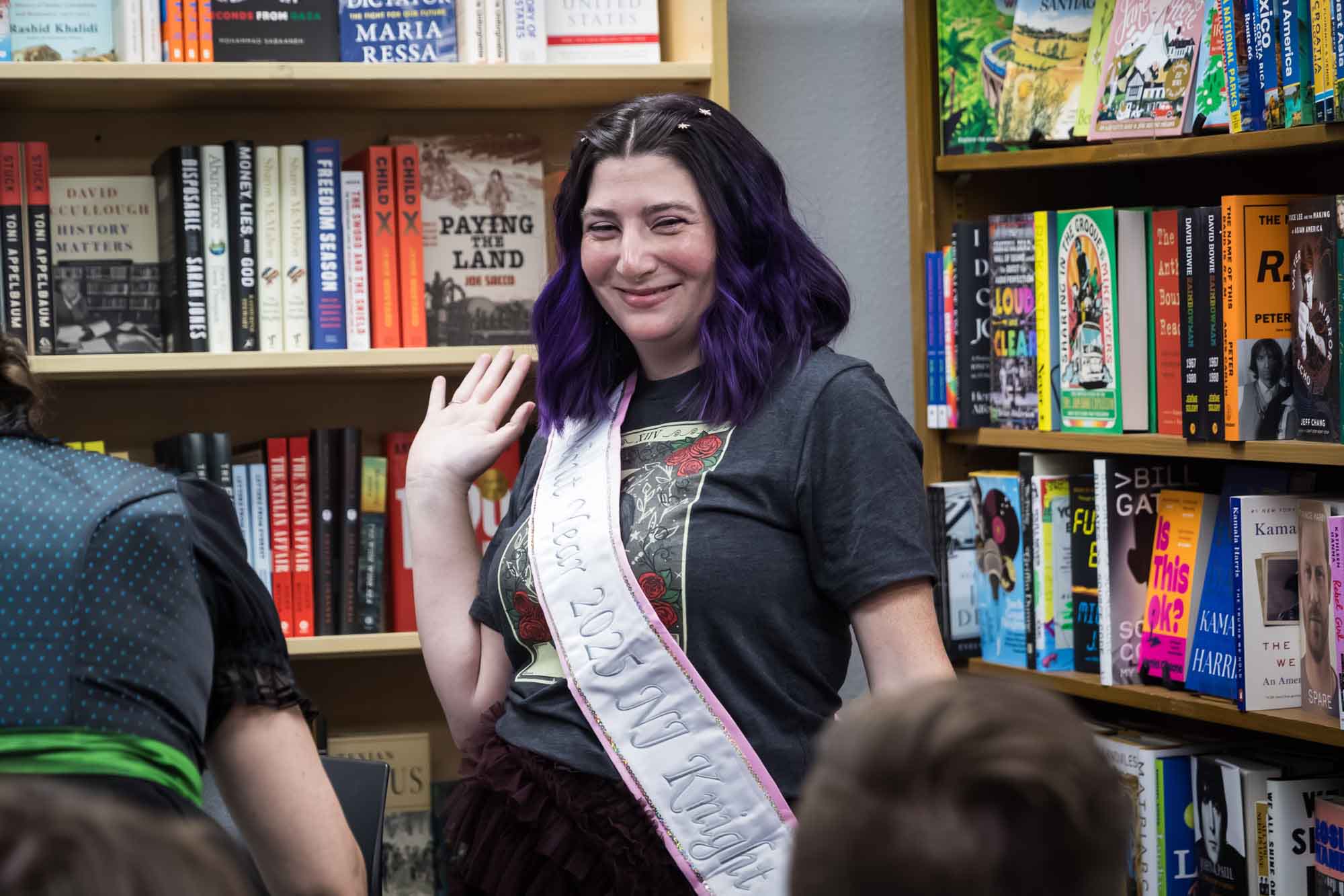 Austin book launch party photos of showing off white and pink sash with hands in air in front of bookshelf filled with books