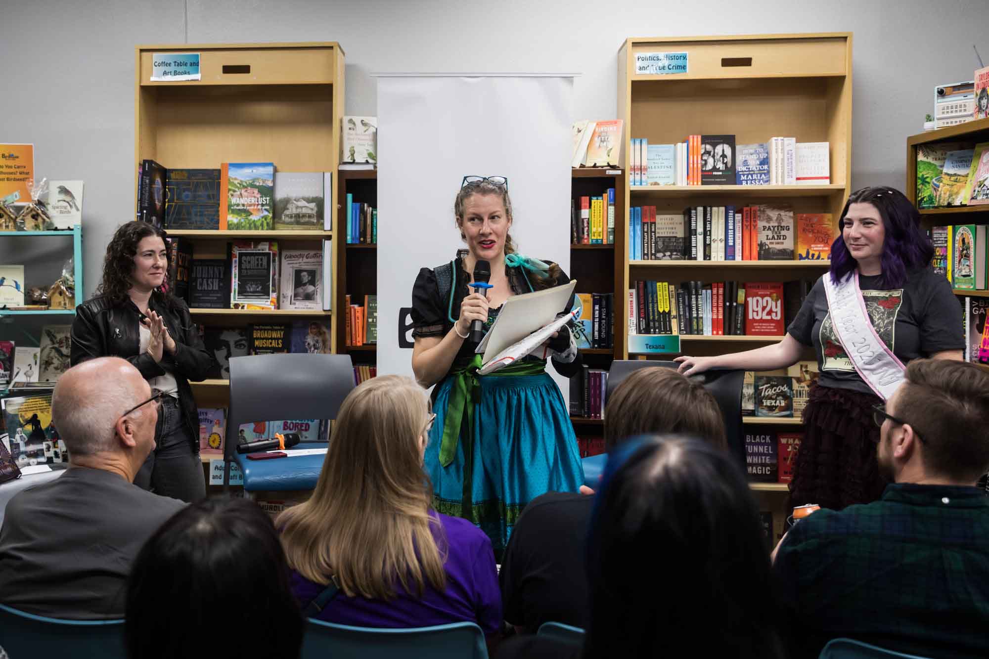 Austin book launch party photos of publisher Britta Jensen talking into microphone in front of authors Erin Cotter and Nancy Knight and guests