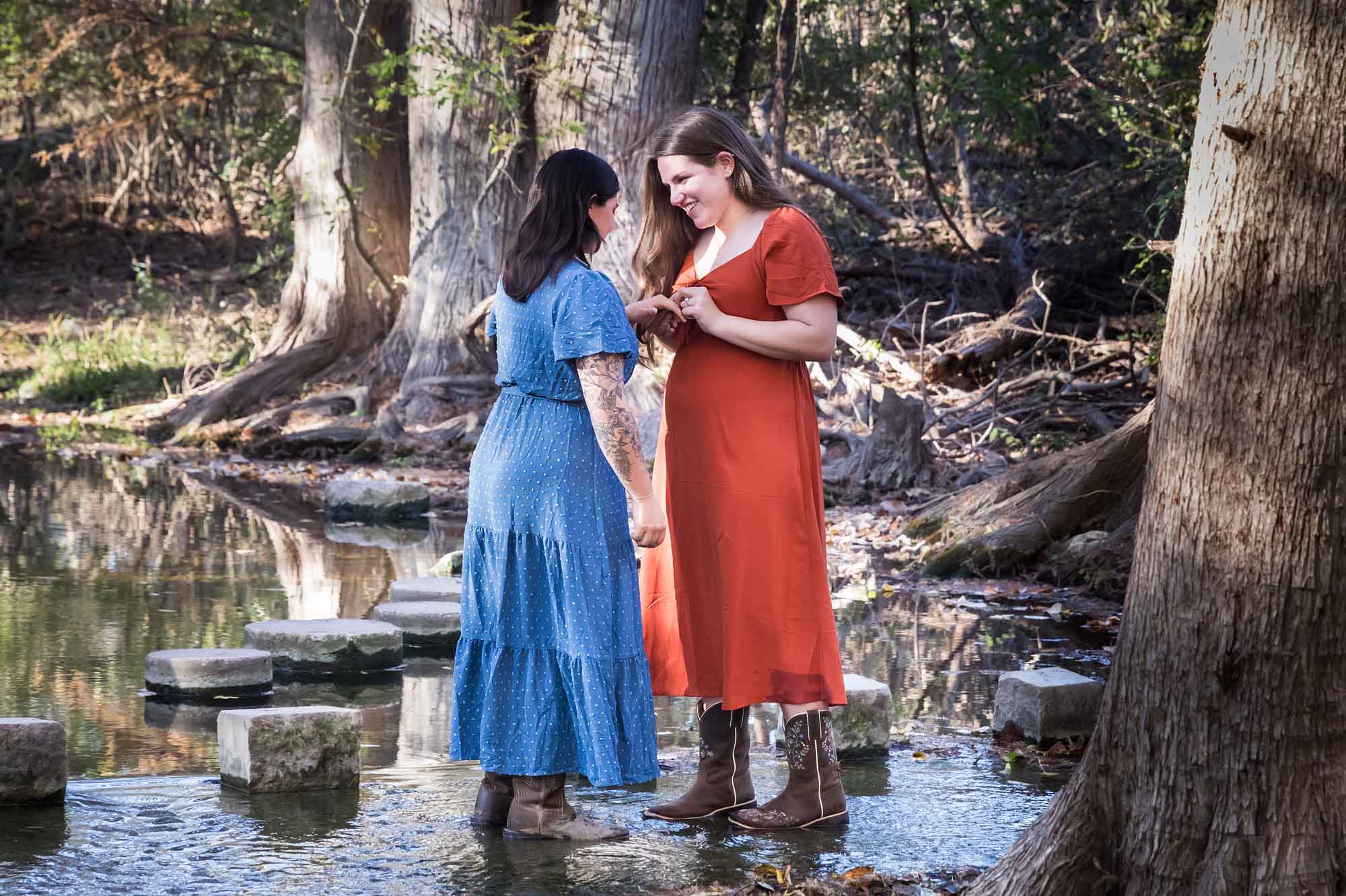 Cibolo Nature Center surprise proposal photos of woman in orange dress putting engagement ring on hand of woman in blue dress in the forest