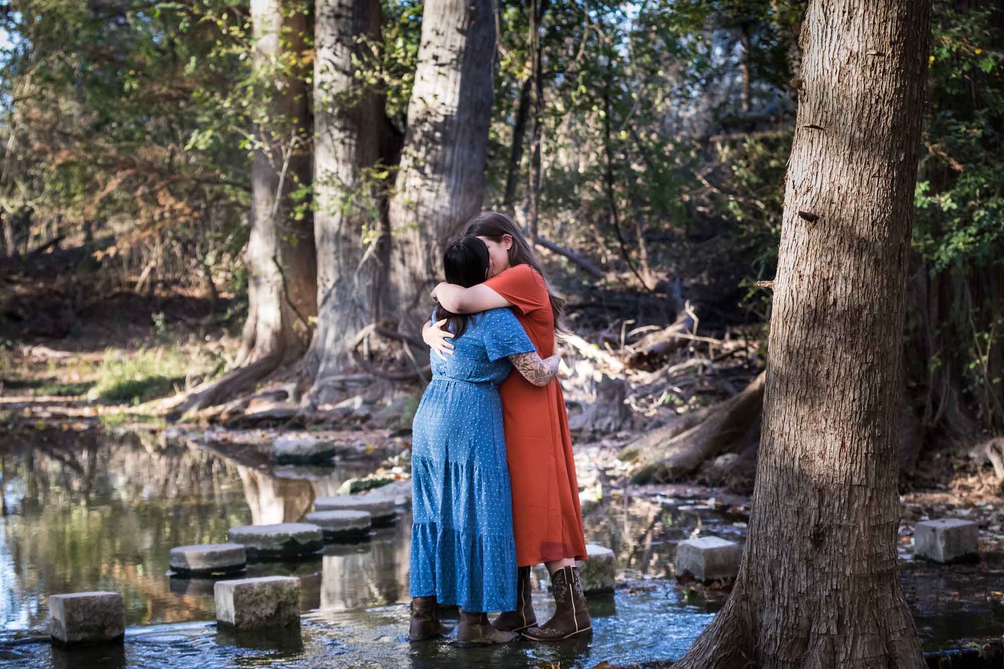 Cibolo Nature Center surprise proposal photos of woman in orange dress kissing woman in blue dress in the forest