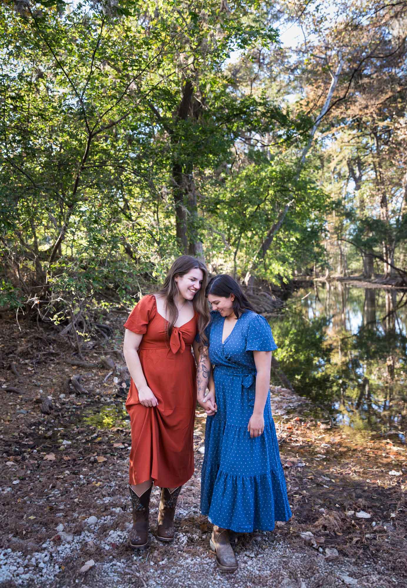 Cibolo Nature Center surprise proposal photos of woman in orange dress and woman in blue dress holding hands in the forest