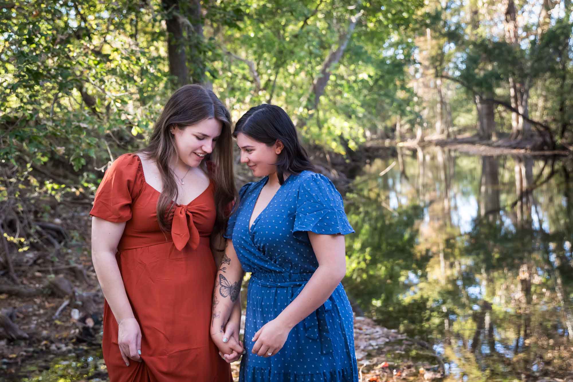 Cibolo Nature Center surprise proposal photos of woman in orange dress and woman in blue dress holding hands in the forest