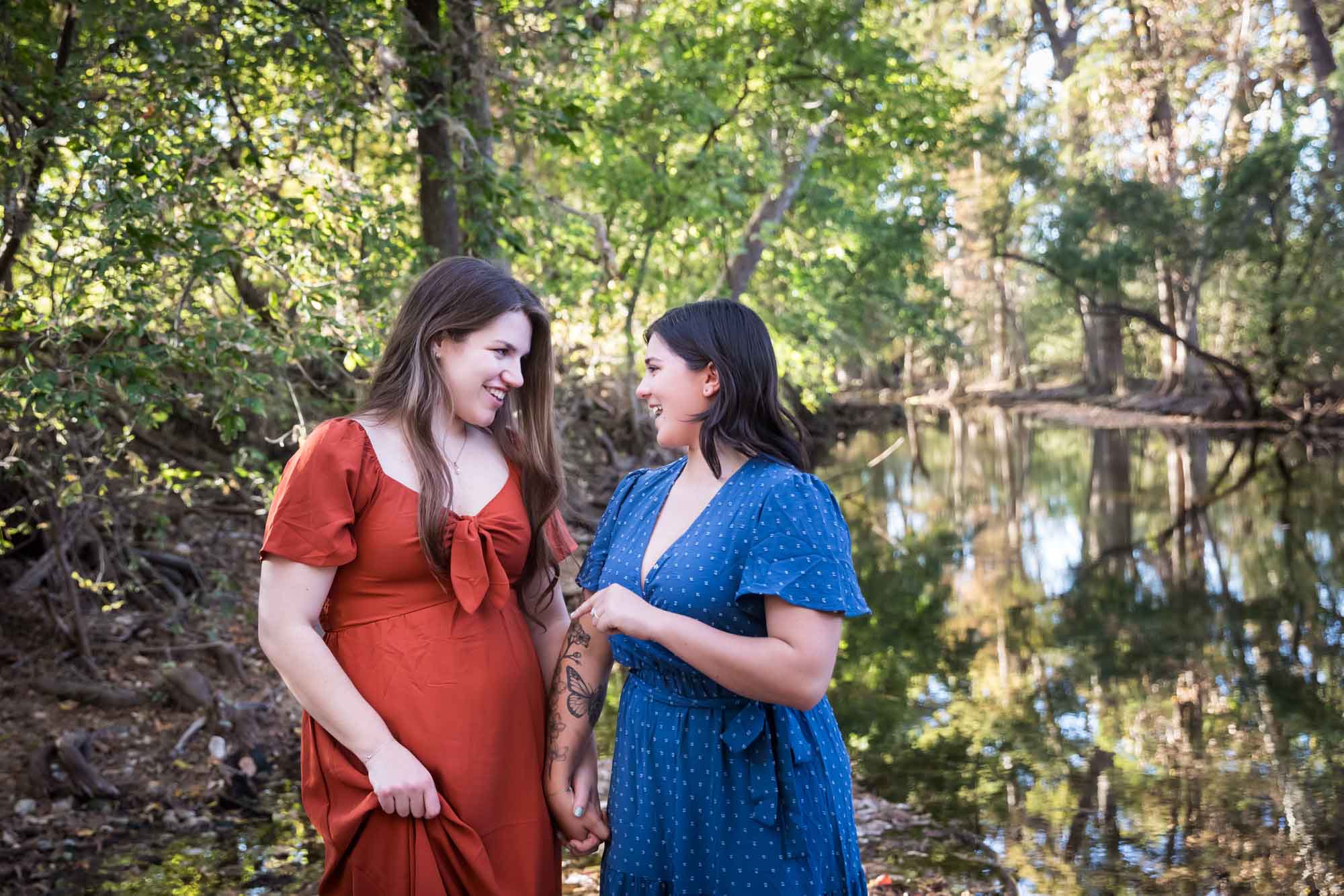 Cibolo Nature Center surprise proposal photos of woman in orange dress and woman in blue dress holding hands in the forest