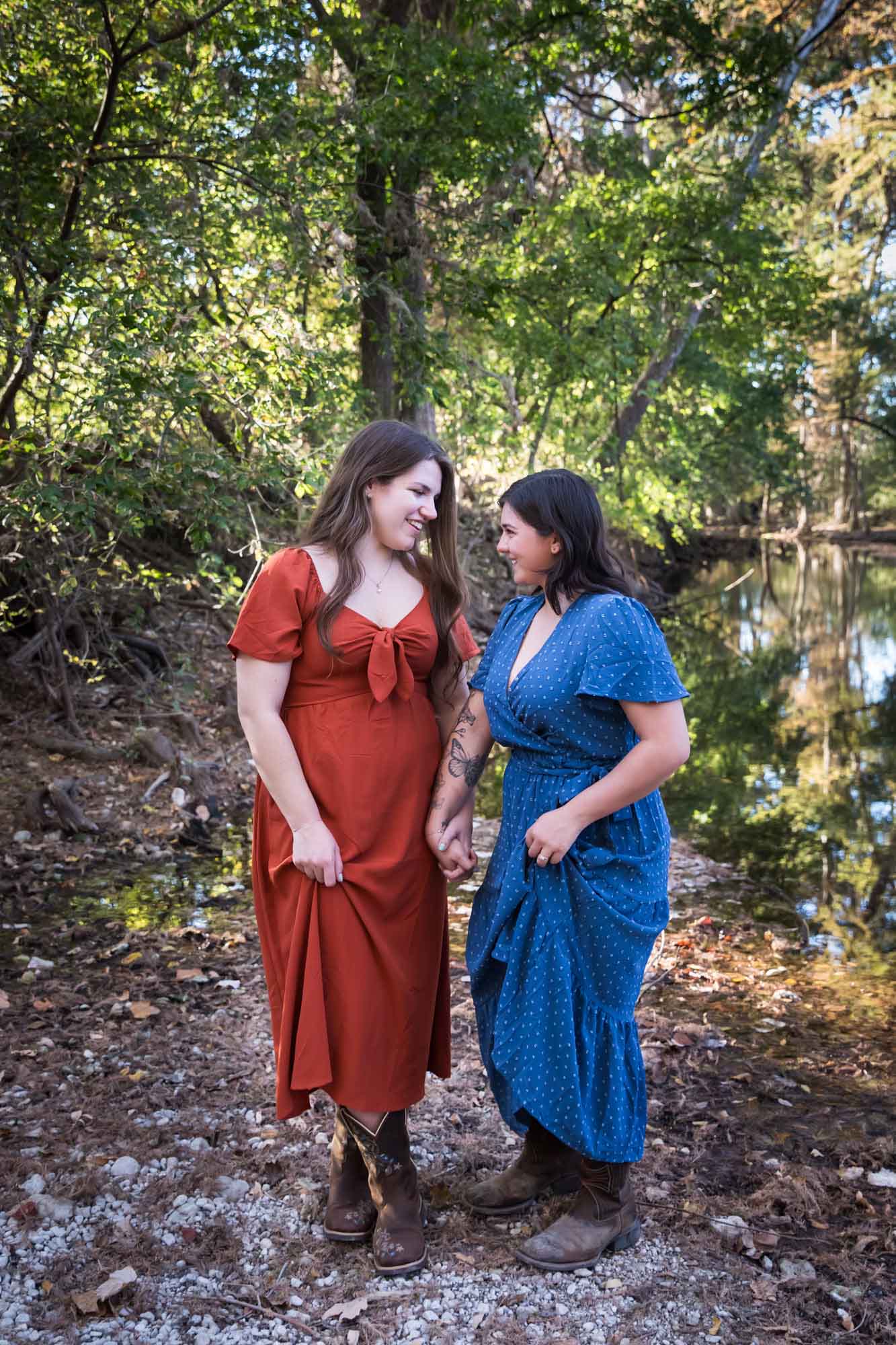 Cibolo Nature Center surprise proposal photos of woman in orange dress and woman in blue dress holding hands in the forest