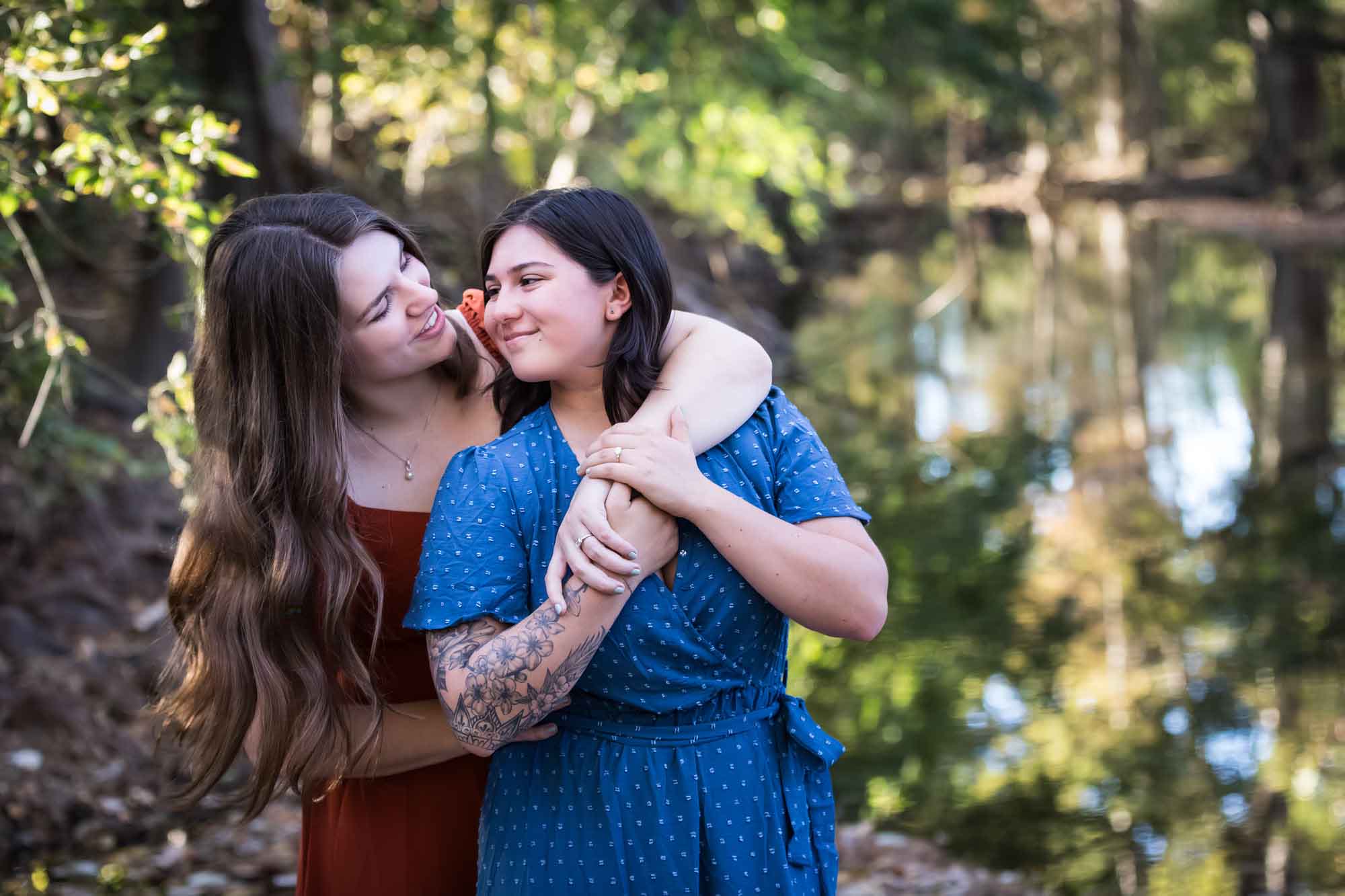 Cibolo Nature Center surprise proposal photos of woman in orange dress hugging woman in blue dress in the forest with Cibolo Creek in background