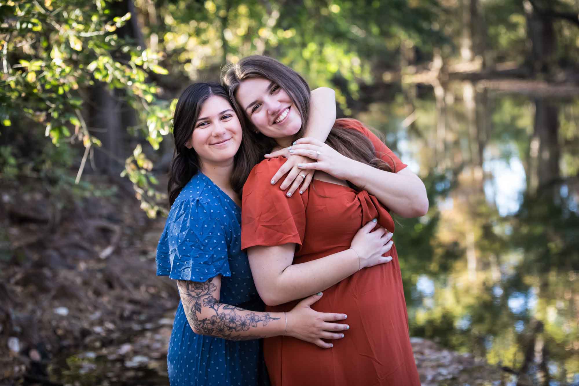 Cibolo Nature Center surprise proposal photos of woman in orange dress hugging woman in blue dress in the forest with Cibolo Creek in background
