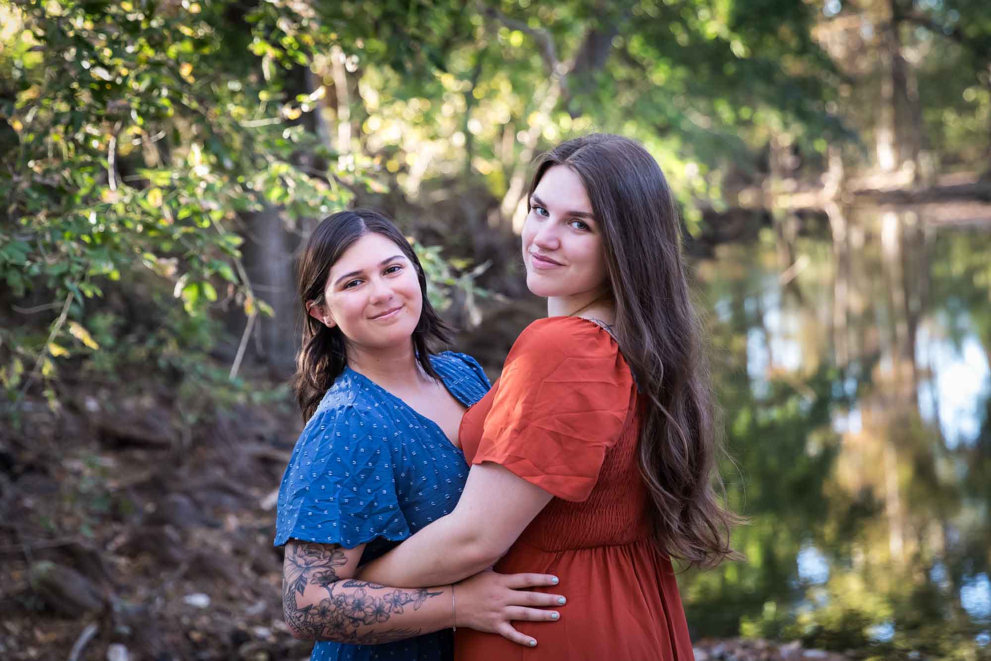 Cibolo Nature Center surprise proposal photos of woman in orange dress hugging woman in blue dress in the forest with Cibolo Creek in background
