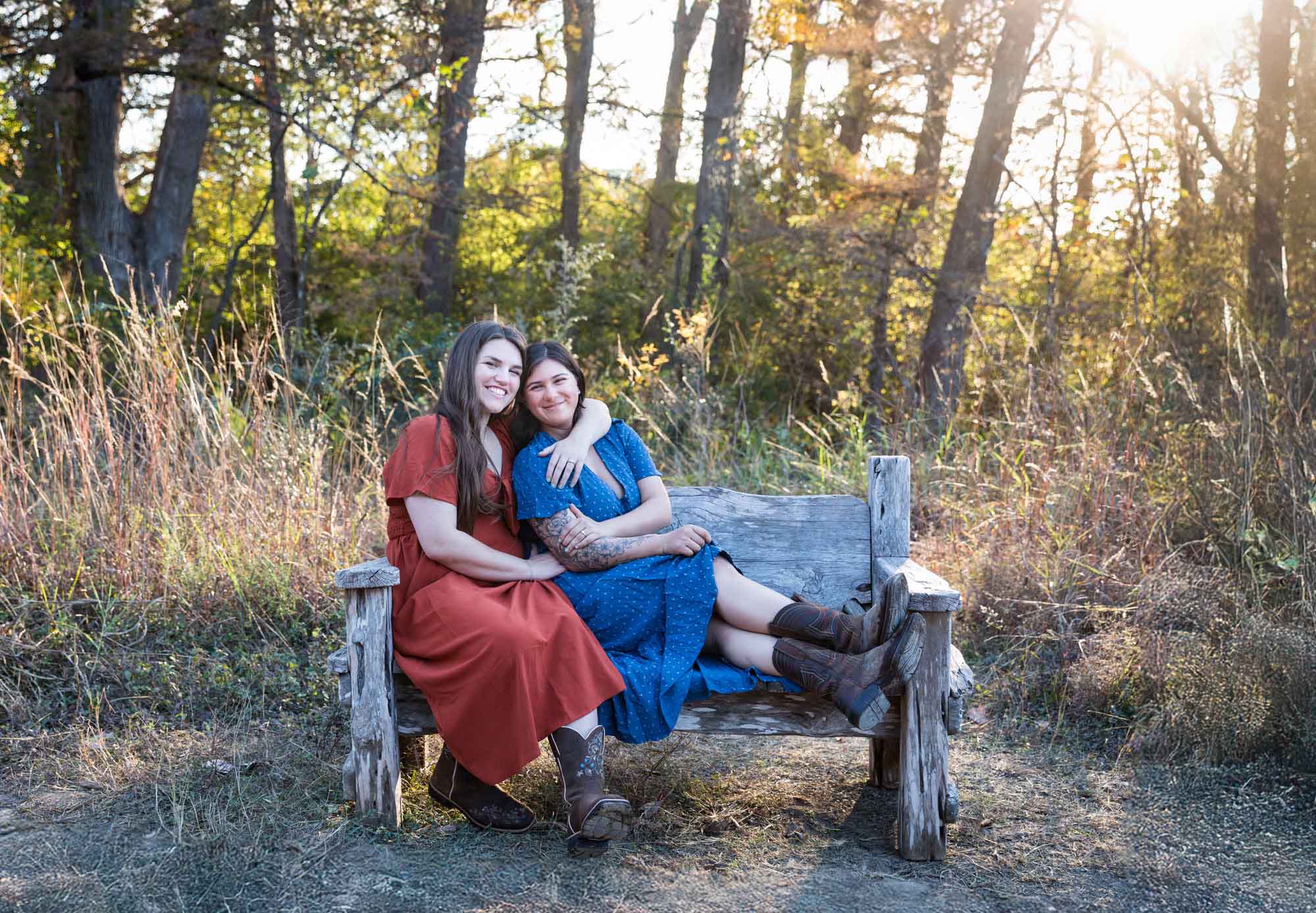 Cibolo Nature Center surprise proposal photos of woman in orange dress hugging woman in blue dress sitting on wooden bench in the forest