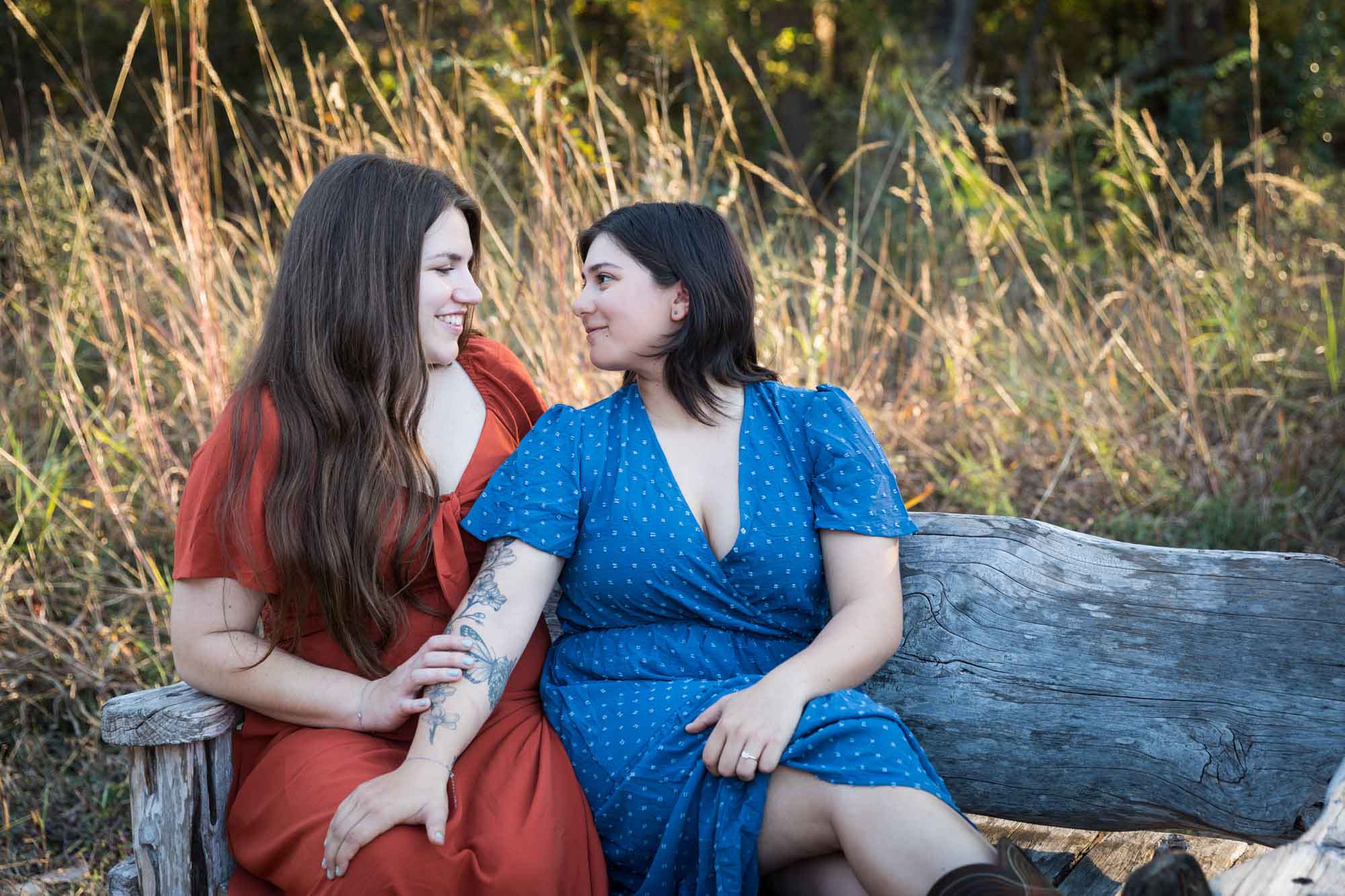 Cibolo Nature Center surprise proposal photos of woman in orange dress hugging woman in blue dress sitting on wooden bench in the forest