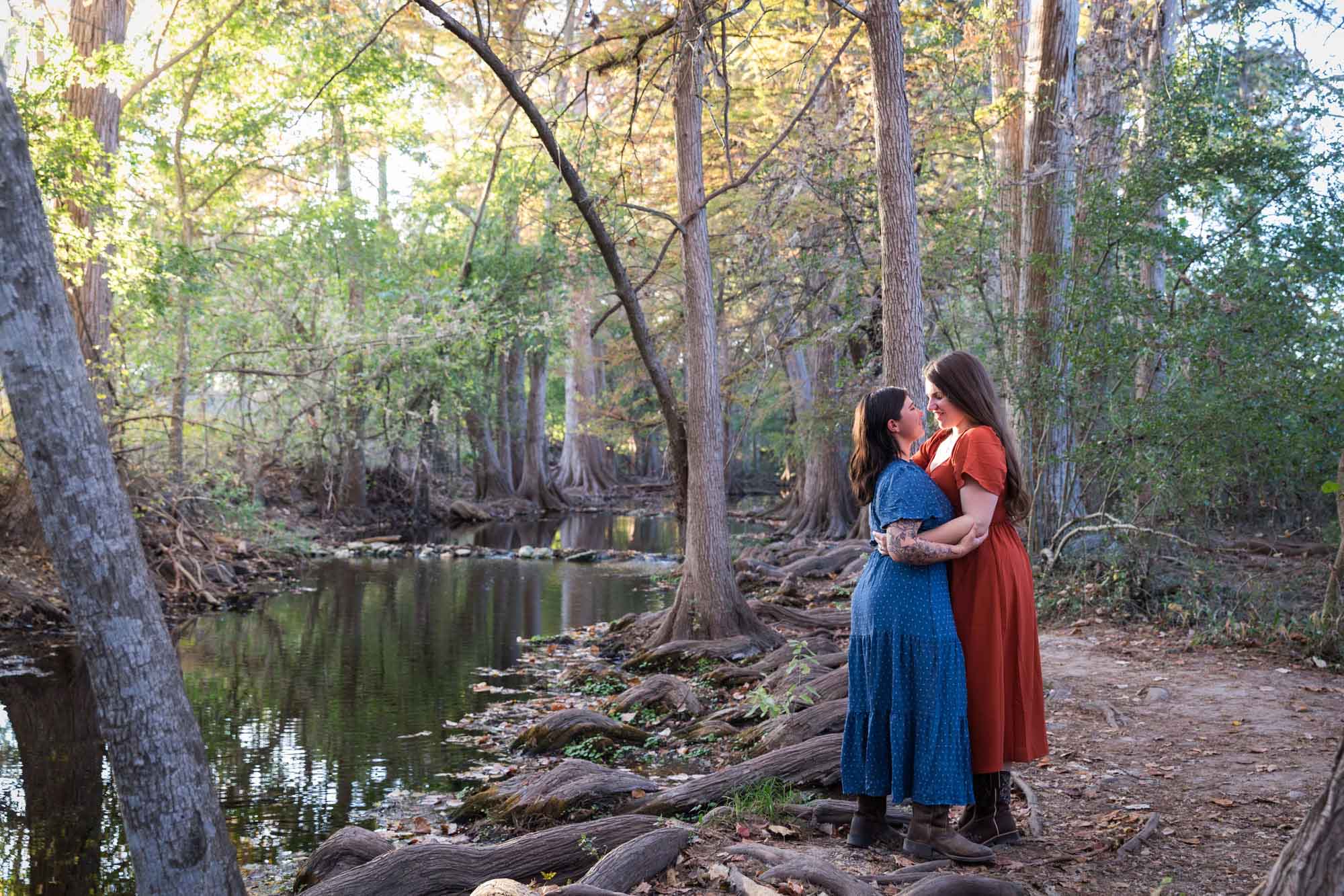 Cibolo Nature Center surprise proposal photos of woman in orange dress hugging woman in blue dress beside Cibolo Creek