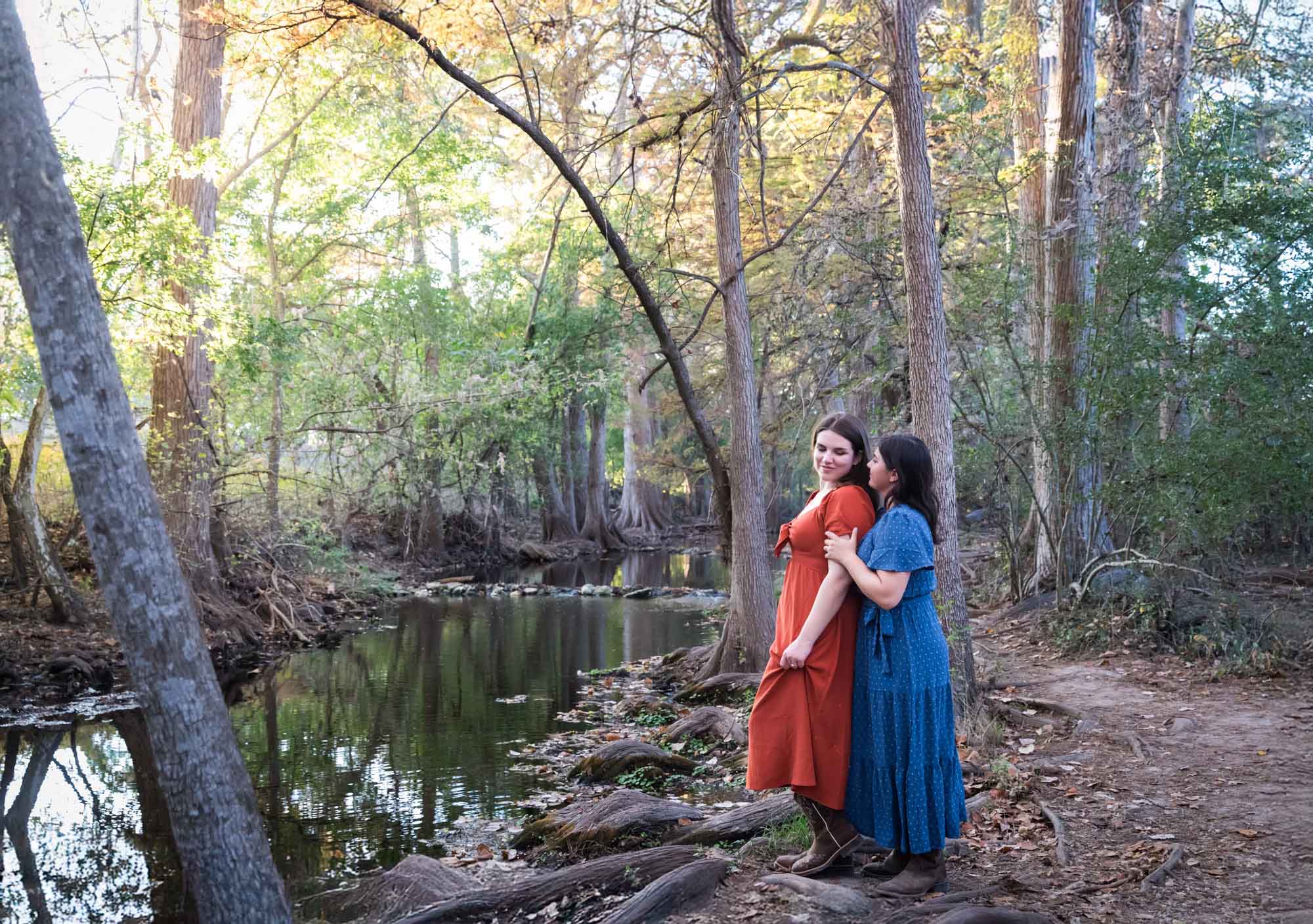 Cibolo Nature Center surprise proposal photos of woman in orange dress hugging woman in blue dress beside Cibolo Creek