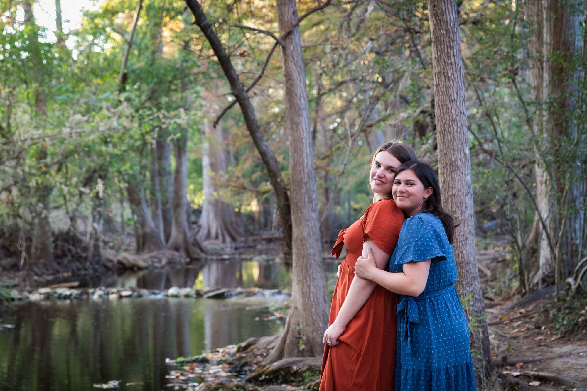 Cibolo Nature Center surprise proposal photos of woman in orange dress hugging woman in blue dress beside Cibolo Creek