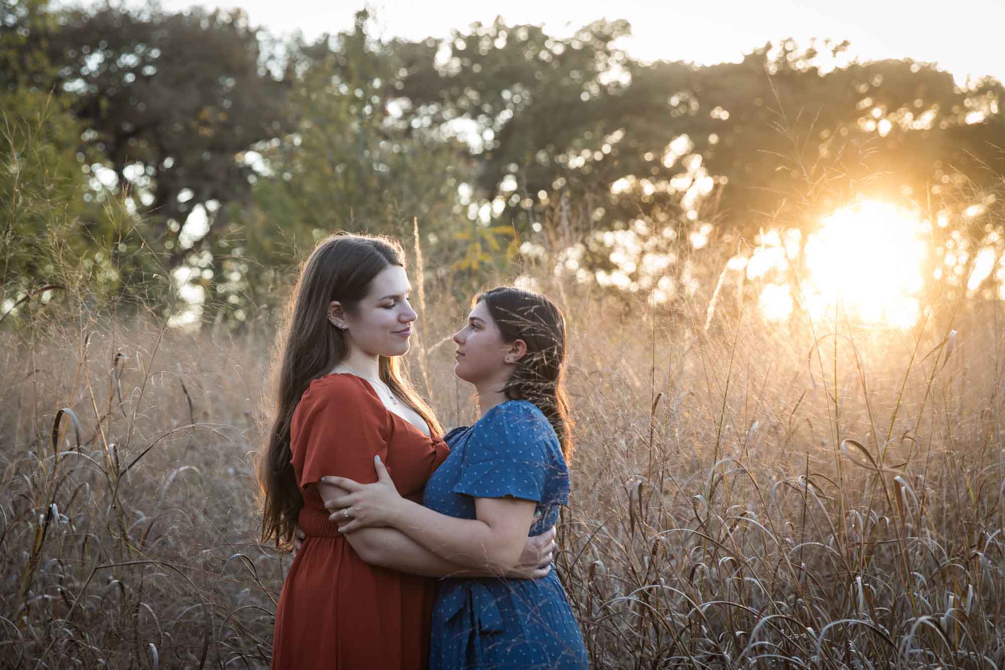 Cibolo Nature Center surprise proposal photos of woman in orange dress hugging woman in blue dress in the middle of marsh grass at sunset