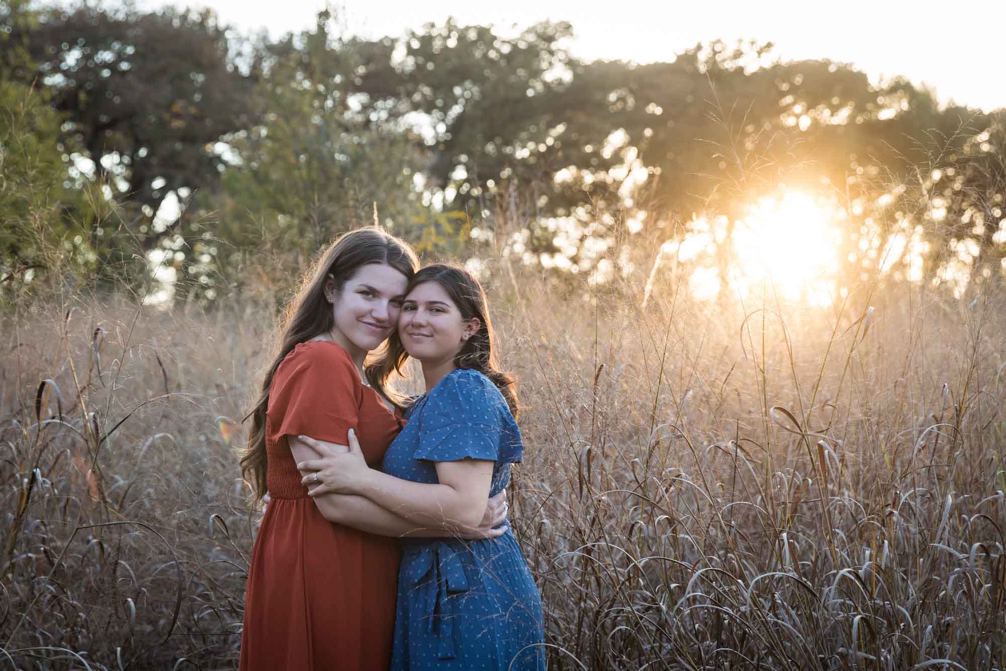 Cibolo Nature Center surprise proposal photos of woman in orange dress hugging woman in blue dress in the middle of marsh grass at sunset