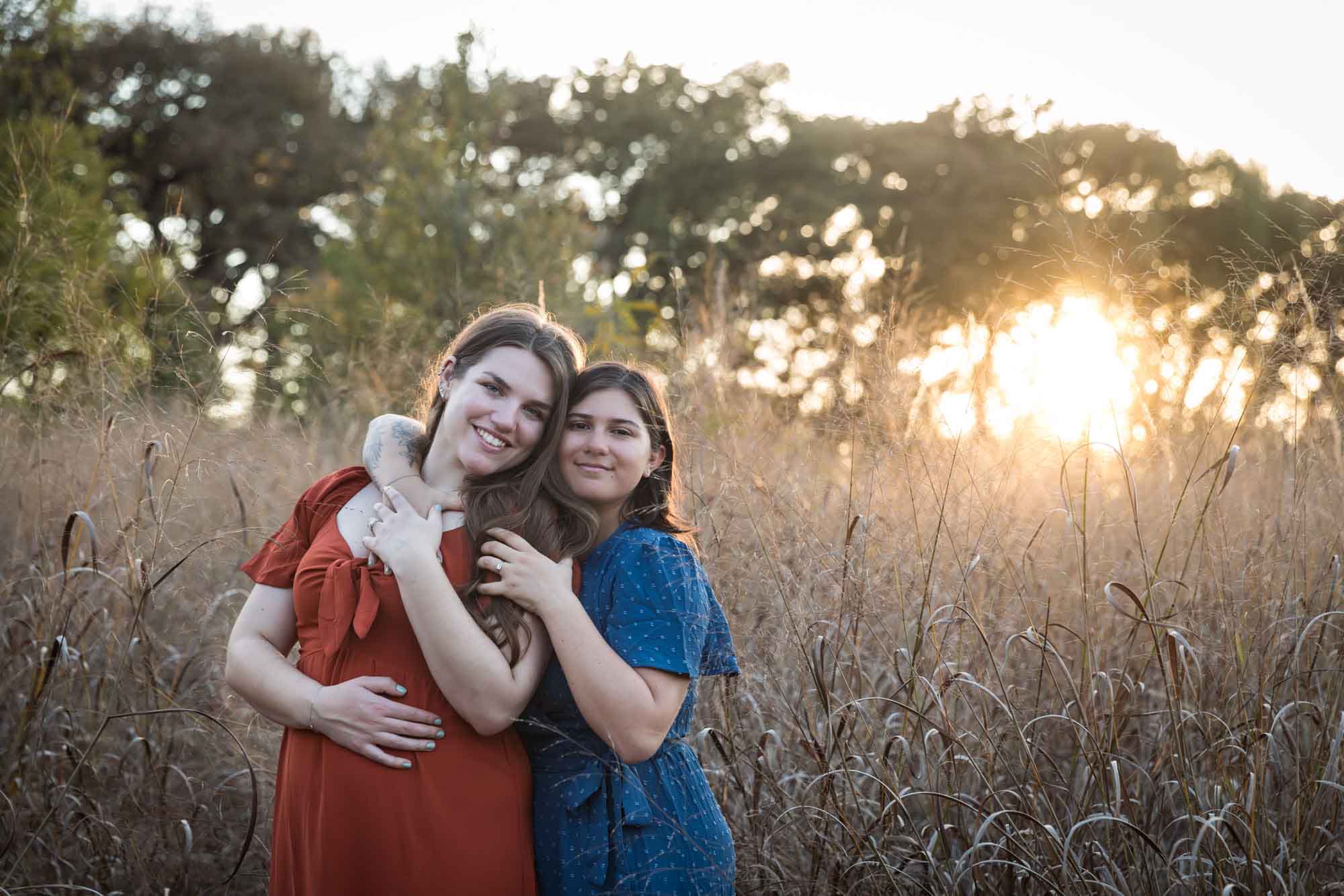Cibolo Nature Center surprise proposal photos of woman in orange dress hugging woman in blue dress in the middle of marsh grass at sunset