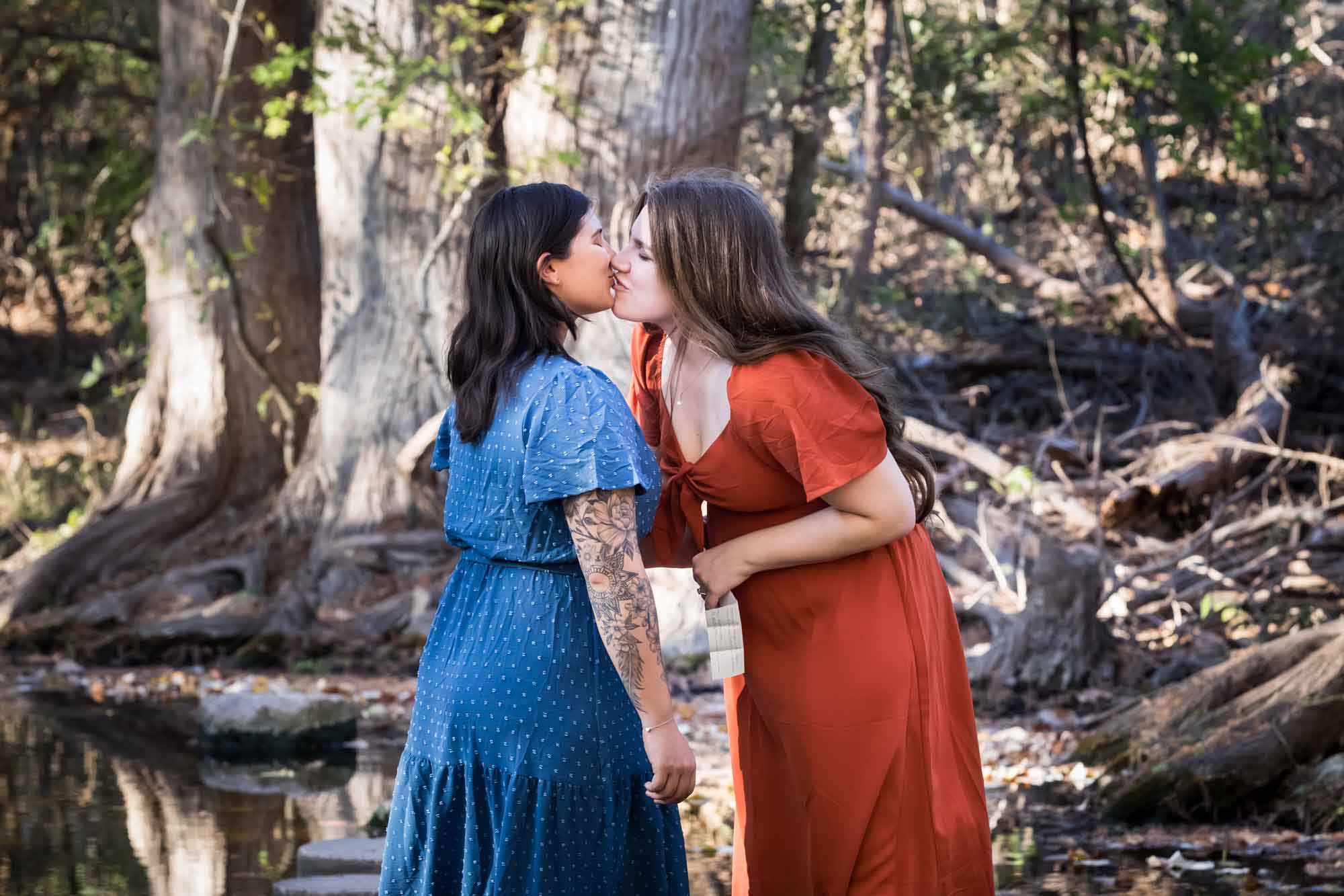Cibolo Nature Center surprise proposal photos of woman in orange dress kissing woman in blue dress in the forest