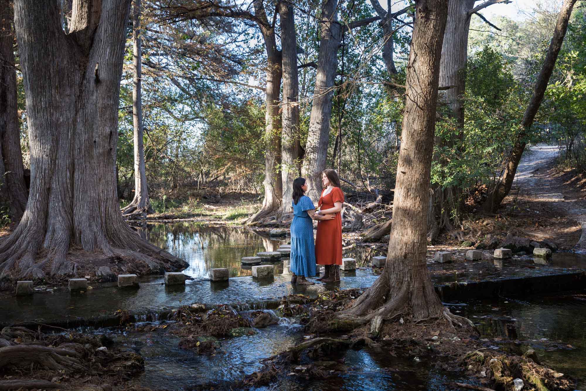 Cibolo Nature Center surprise proposal photos of woman in orange dress standing in front of woman in blue dress in the forest