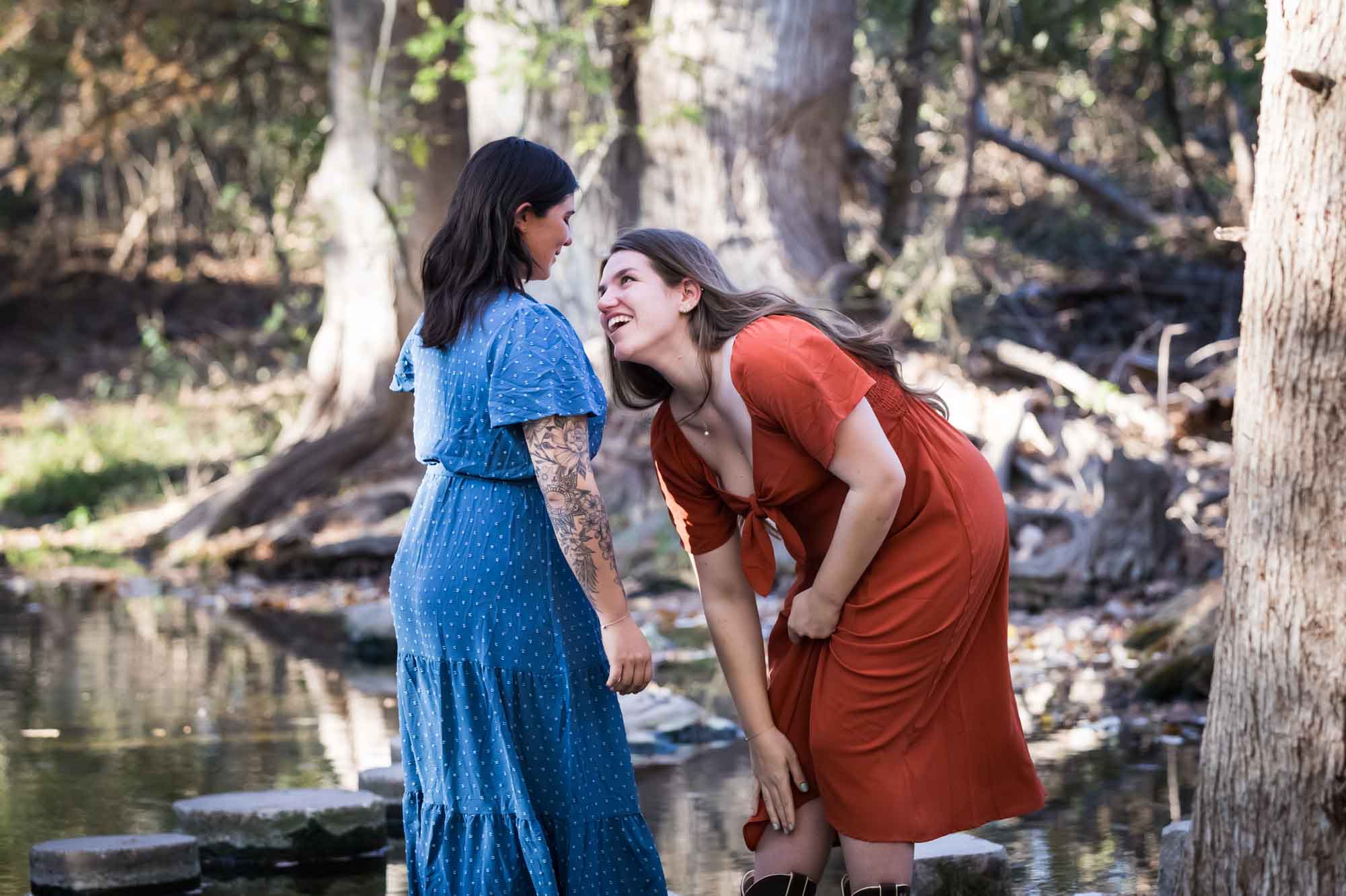 Cibolo Nature Center surprise proposal photos of woman in orange dress reaching down into boot standing in front of woman in blue dress in the forest