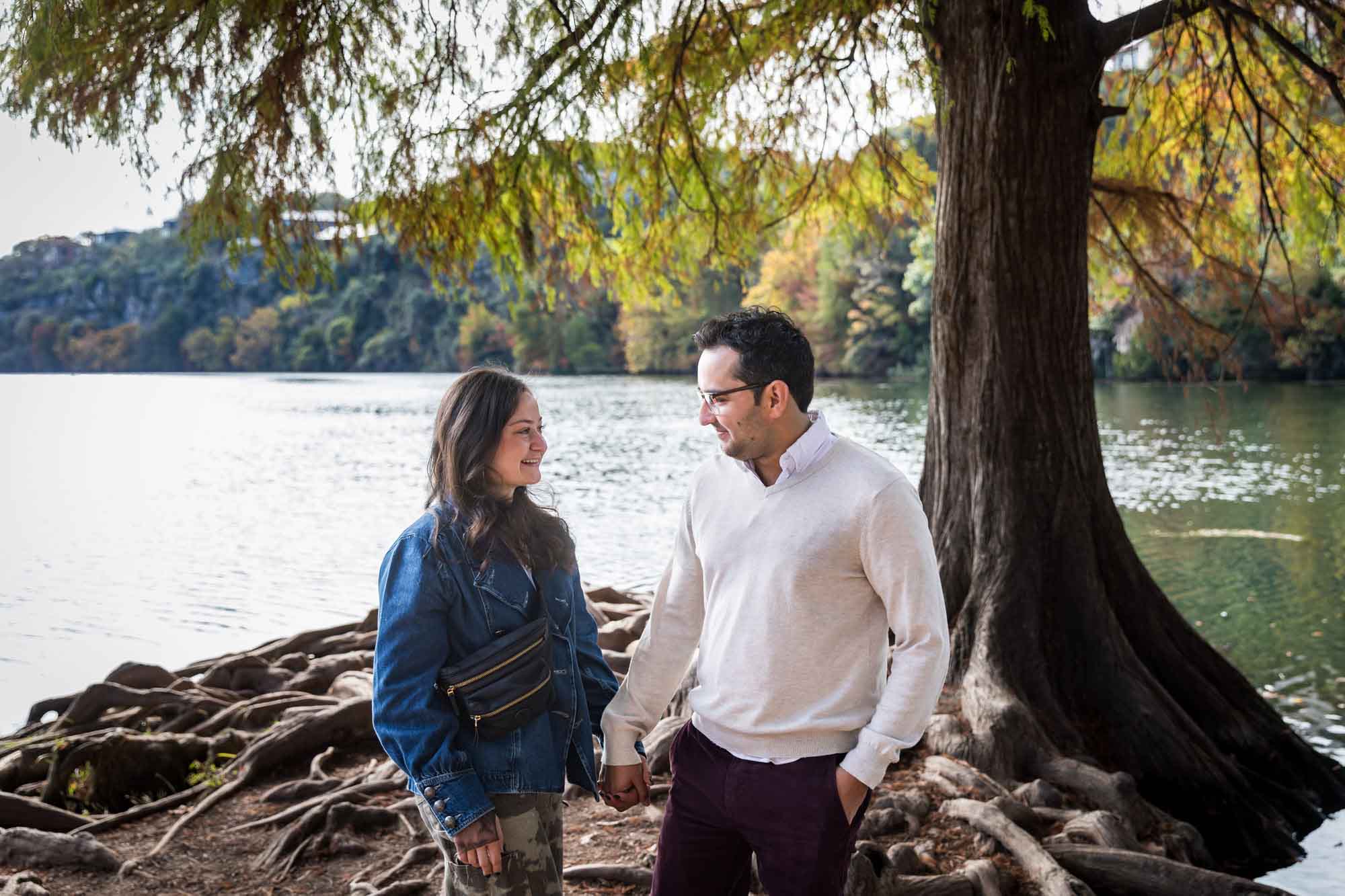 Man wearing maroon pants and white shirt holding hands with woman wearing camo pants and denim jacket at end of island with tree in background during a Red Bud Isle surprise proposal