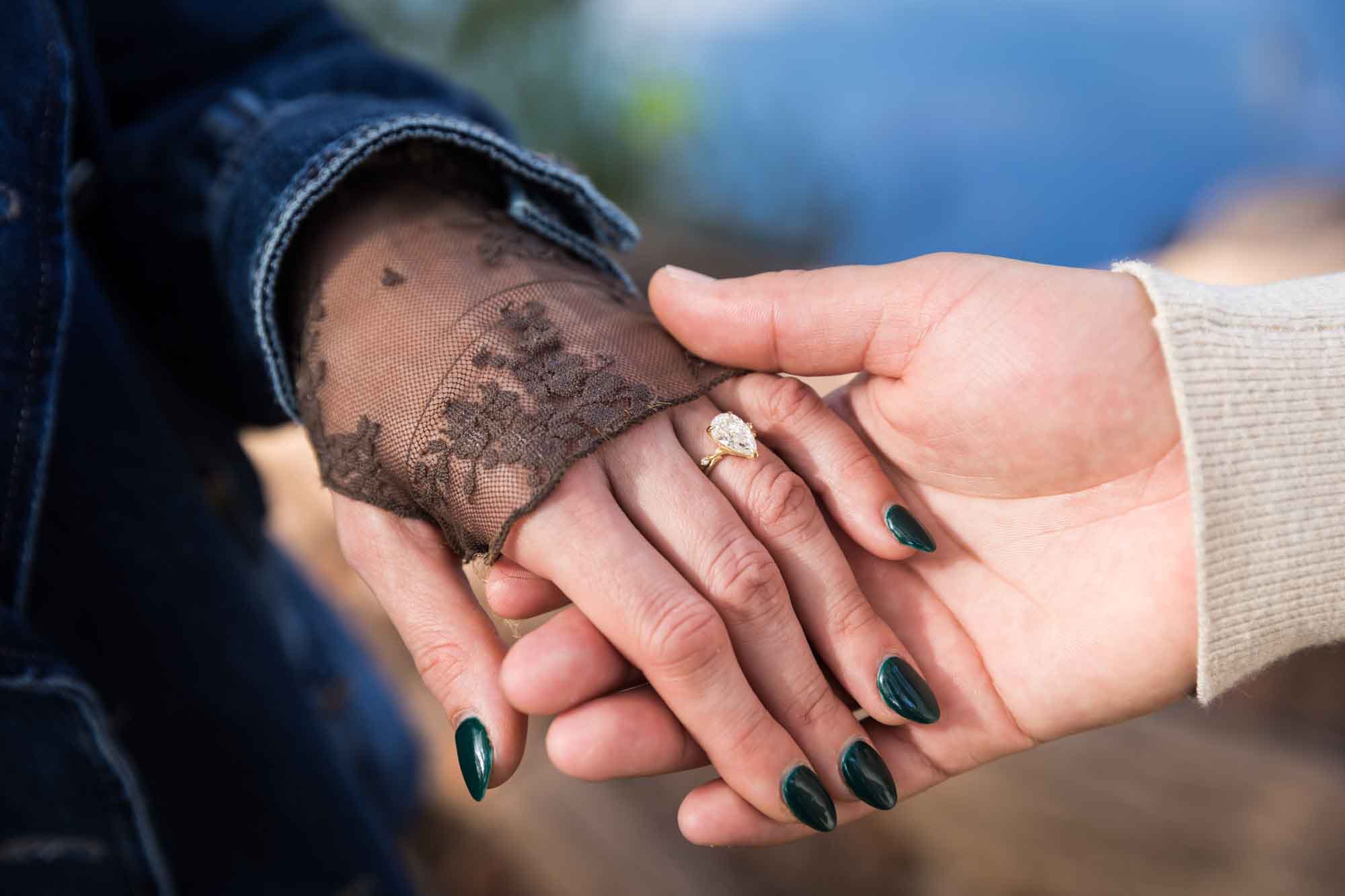 Close up of man holding woman's hand covered in black lace and showing pear-cut engagement ring