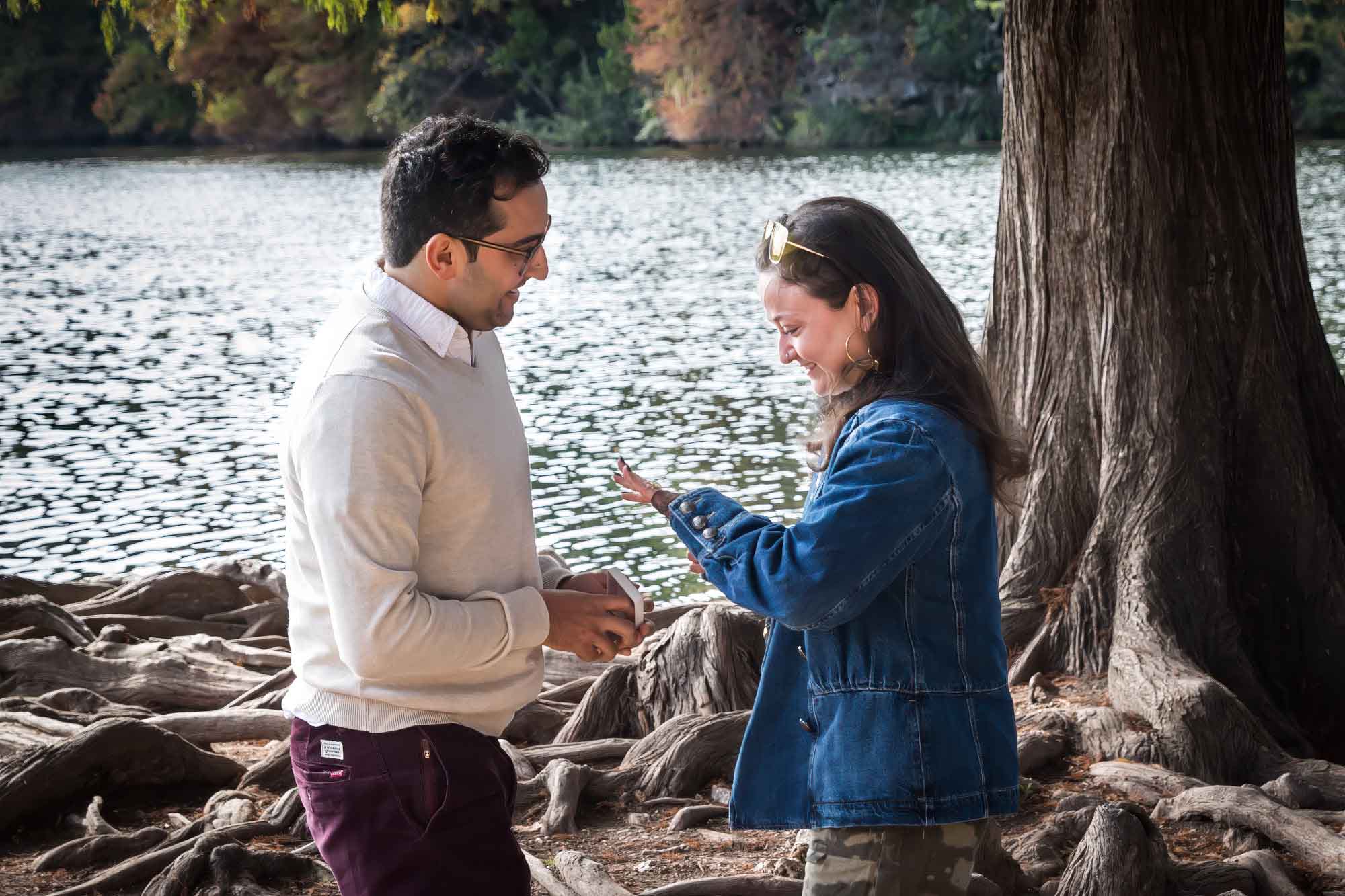 Man wearing maroon pants and white shirt standing in front of woman wearing camo pants and denim jacket at end of island with tree in background during a Red Bud Isle surprise proposal
