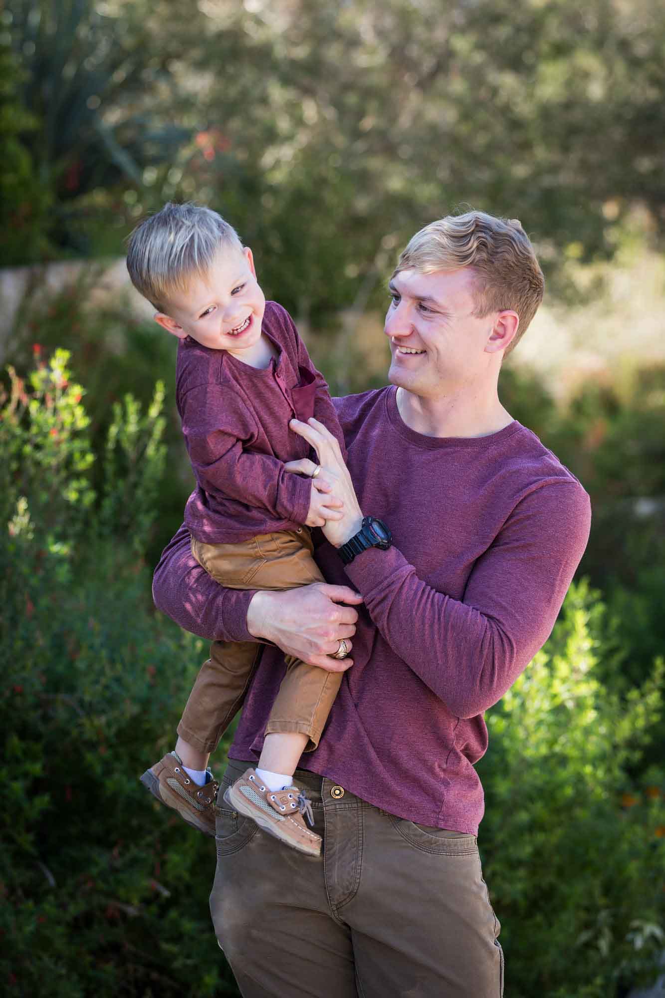 San Antonio Botanical Gardens family portrait of man wearing purple shirt and brown pants playing with little boy wearing purple shirt and tan pants
