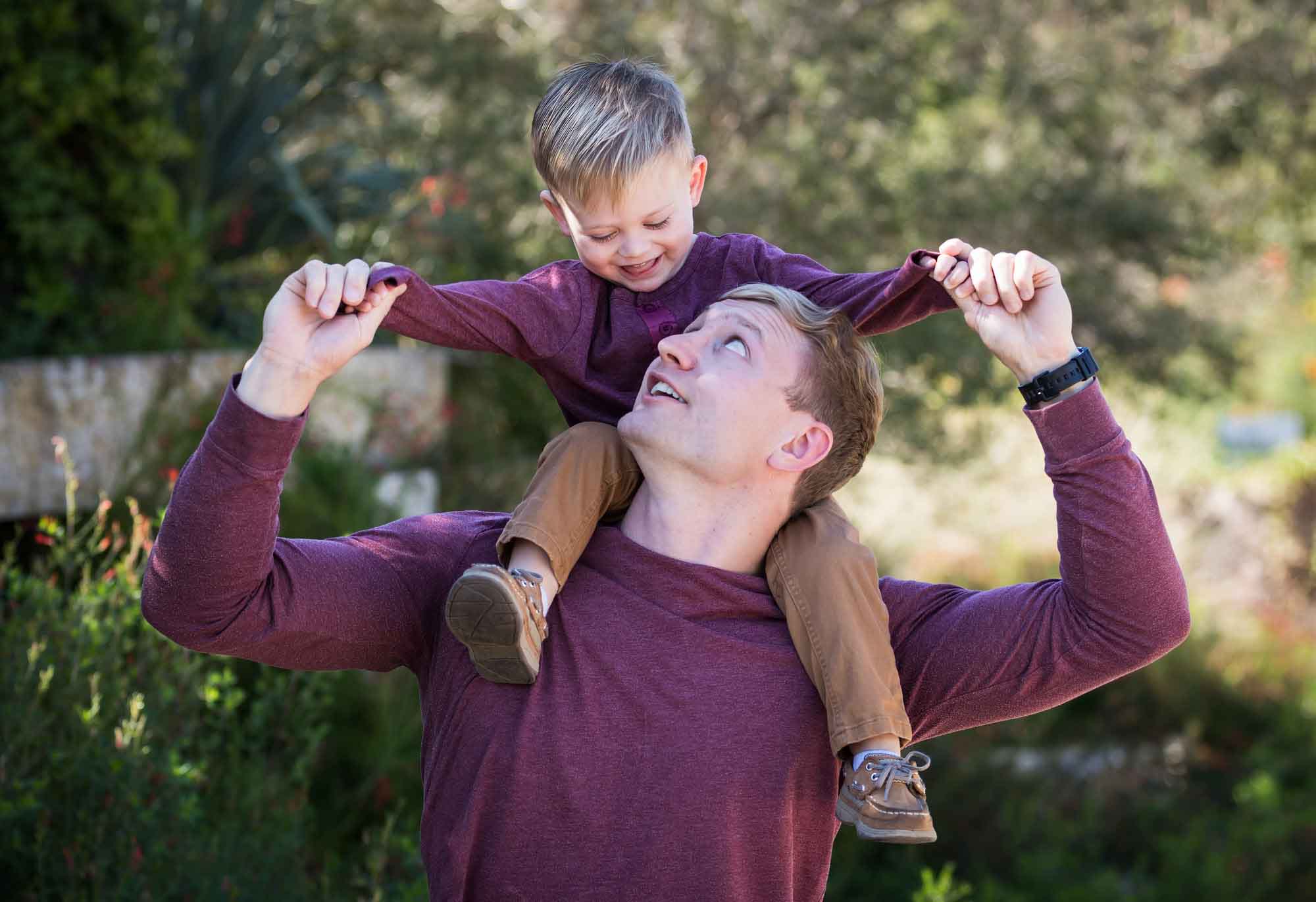 San Antonio Botanical Gardens family portrait of man wearing purple shirt and brown pants holding little boy wearing purple shirt and tan pants on his shoulders
