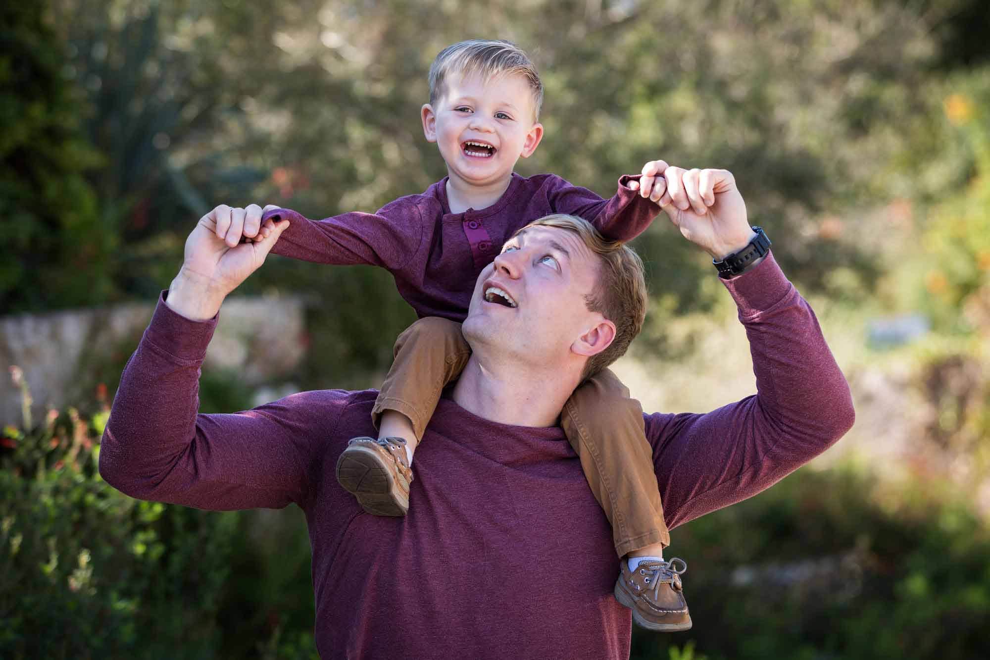 San Antonio Botanical Gardens family portrait of man wearing purple shirt and brown pants holding little boy wearing purple shirt and tan pants on his shoulders