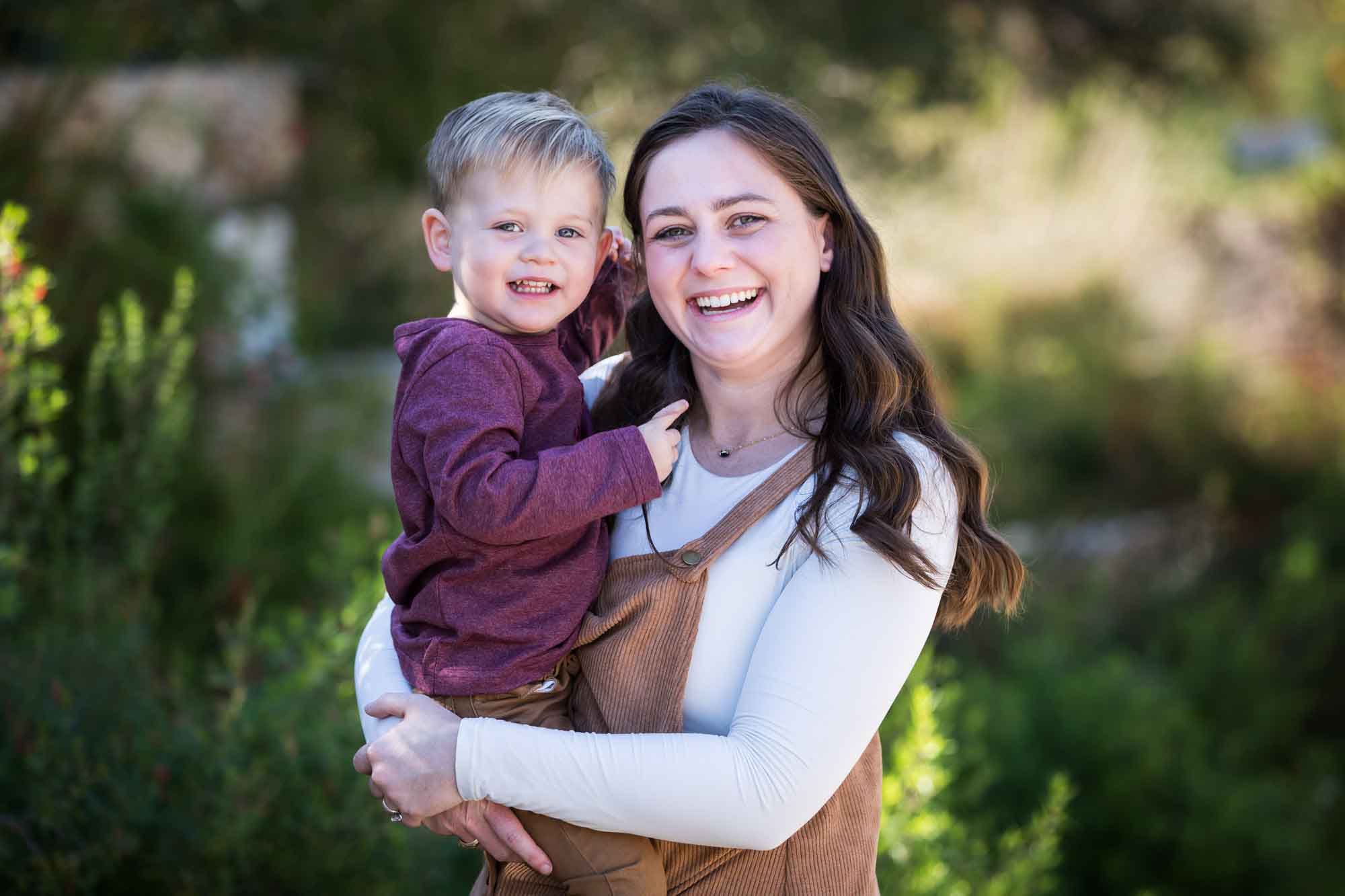 San Antonio Botanical Gardens family portrait of woman wearing white shirt and corduroy dress holding little boy wearing purple shirt and tan pants