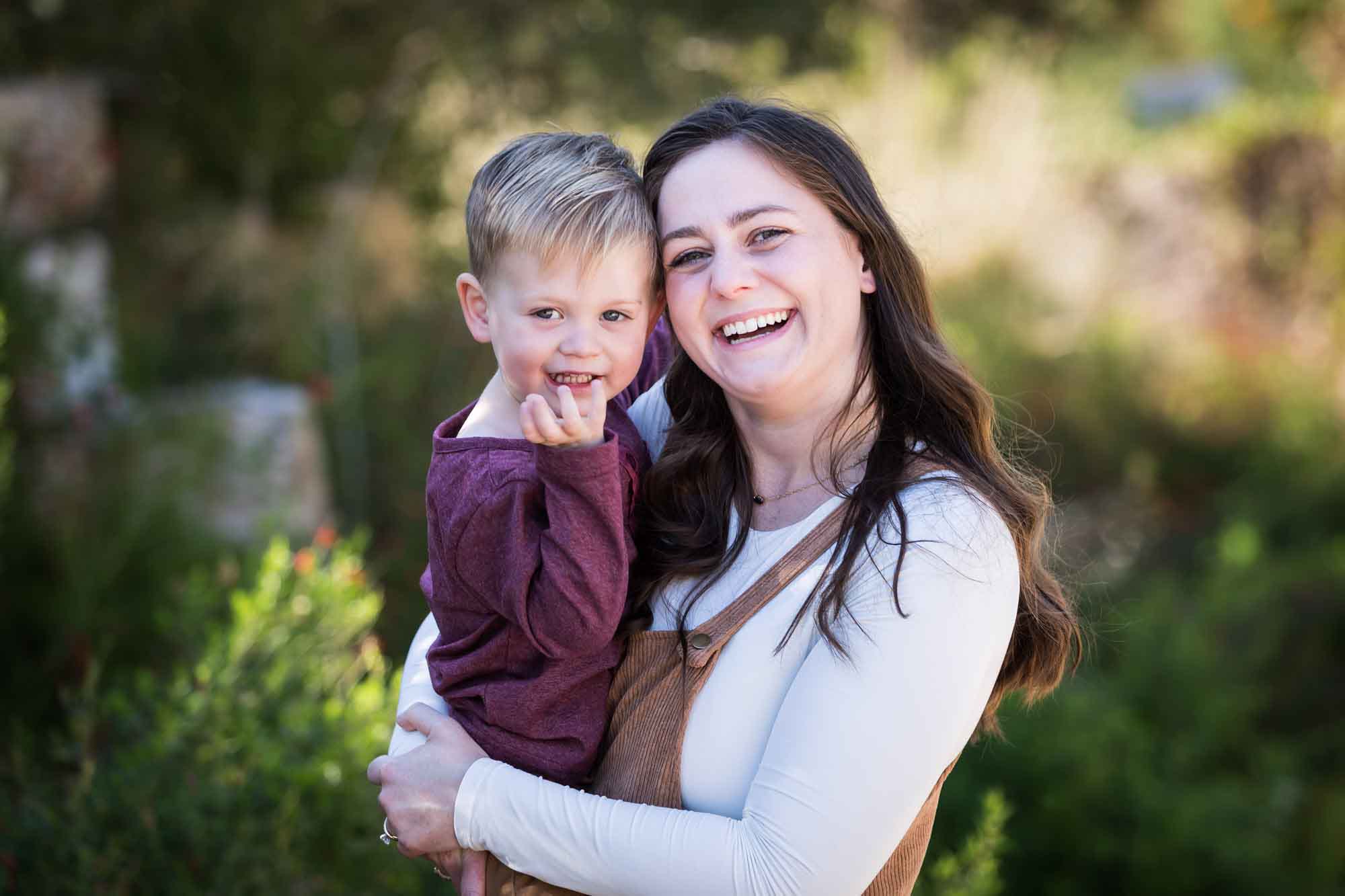 San Antonio Botanical Gardens family portrait of woman wearing white shirt and corduroy dress holding little boy wearing purple shirt and tan pants