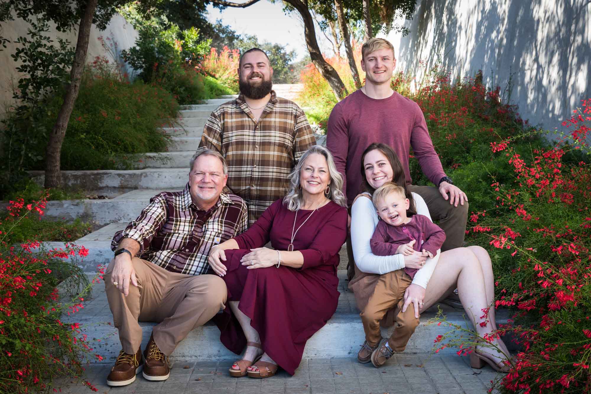 San Antonio Botanical Gardens family portrait of family of grandparents, mother, father, and brother plus little boy sitting together on steps with bushes on side