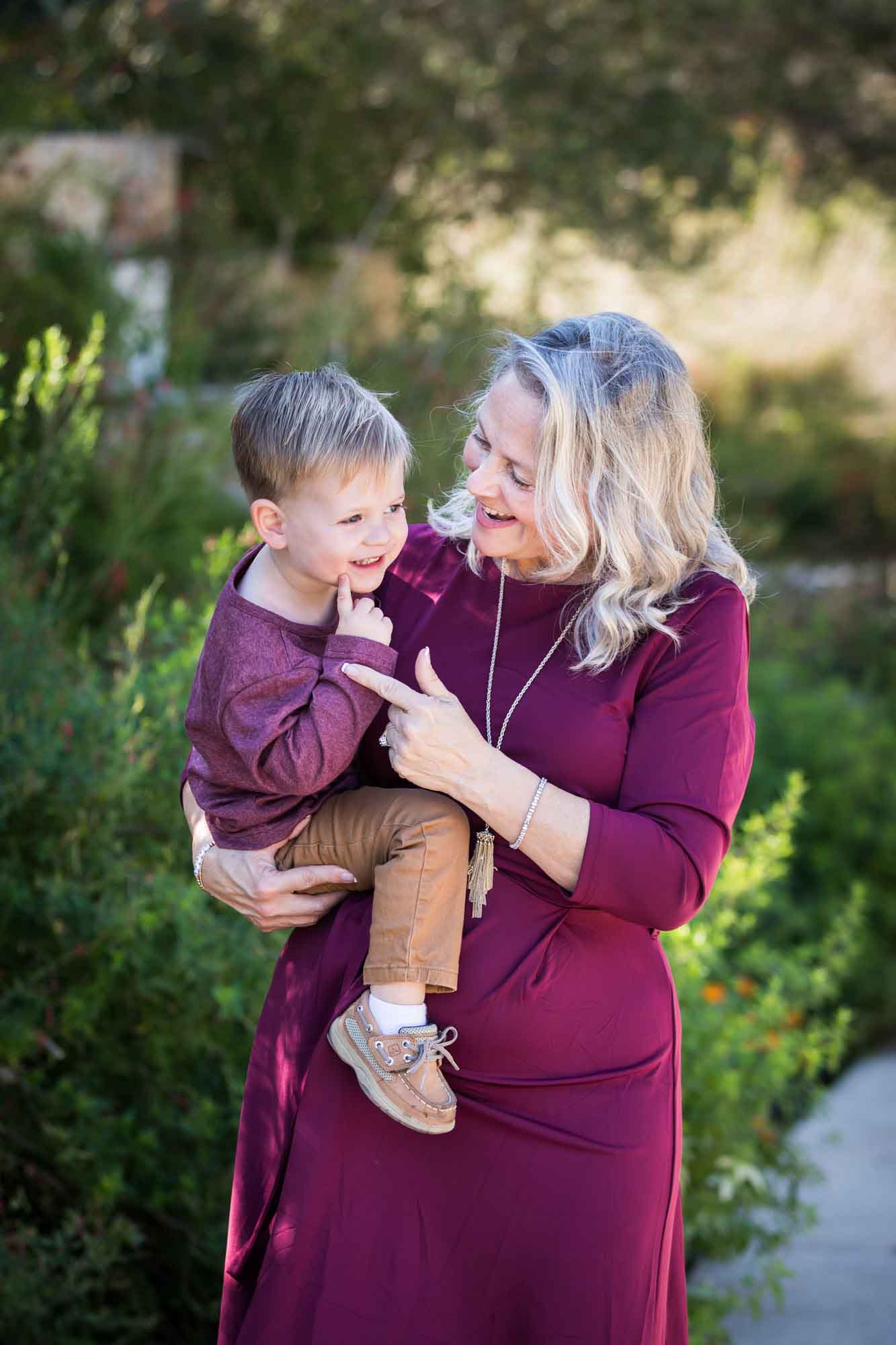 San Antonio Botanical Gardens family portrait of grandmother wearing maroon dress playing with little boy wearing purple shirt and tan pants