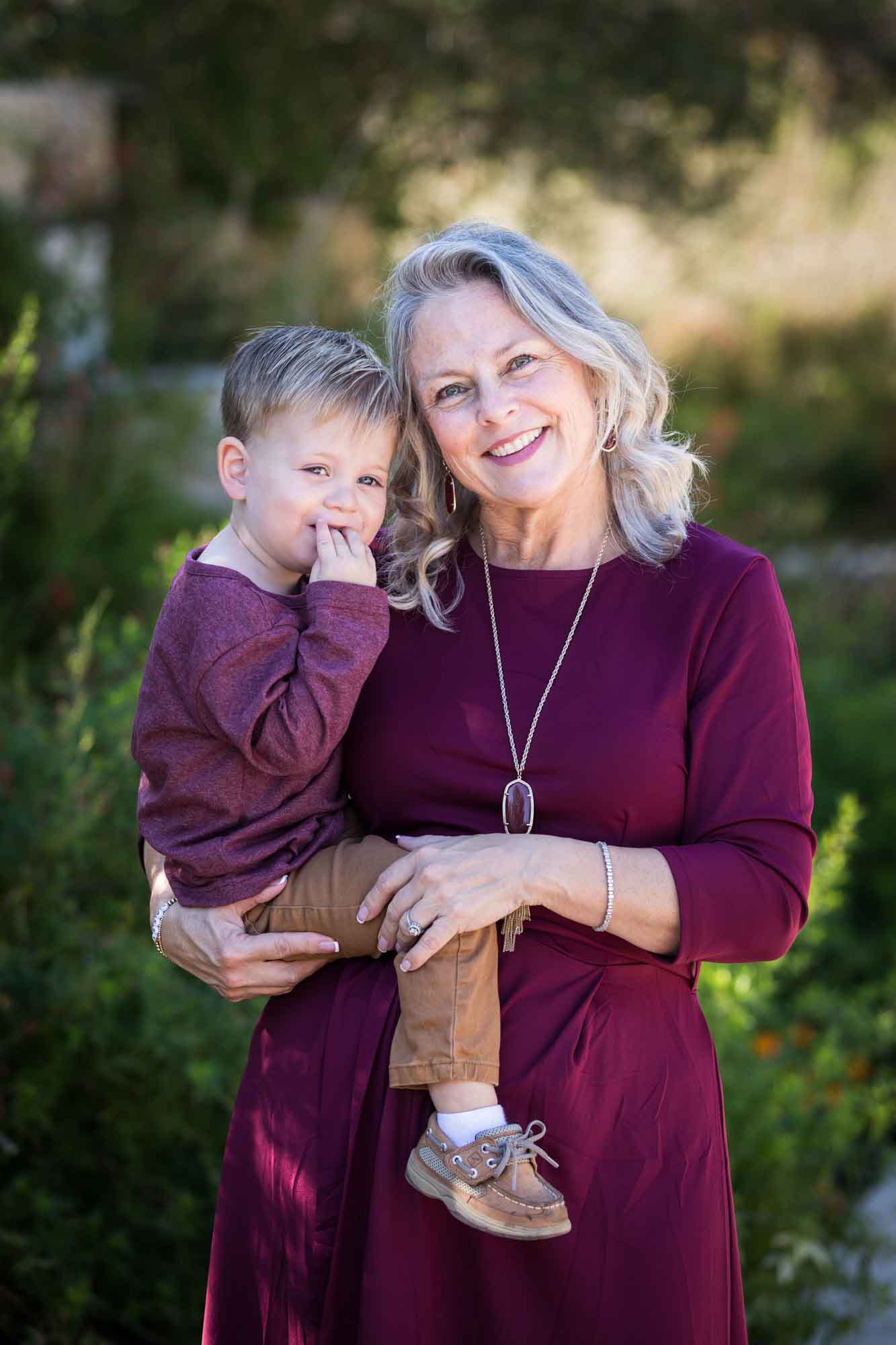 San Antonio Botanical Gardens family portrait of grandmother wearing maroon dress holding little boy wearing purple shirt and tan pants