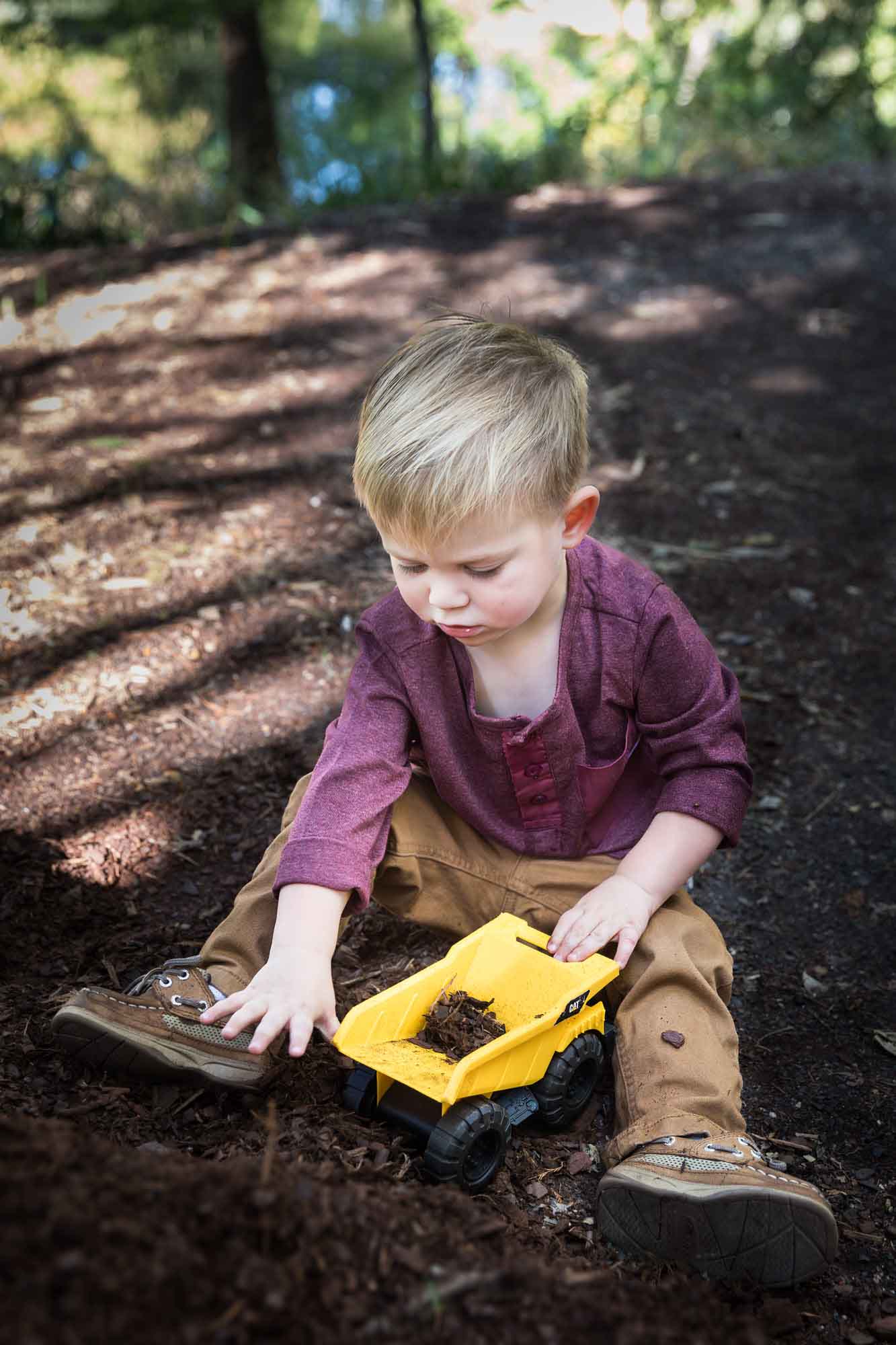 San Antonio Botanical Gardens family portrait of little boy wearing maroon shirt and khaki pants playing with mulch in his toy dump truck