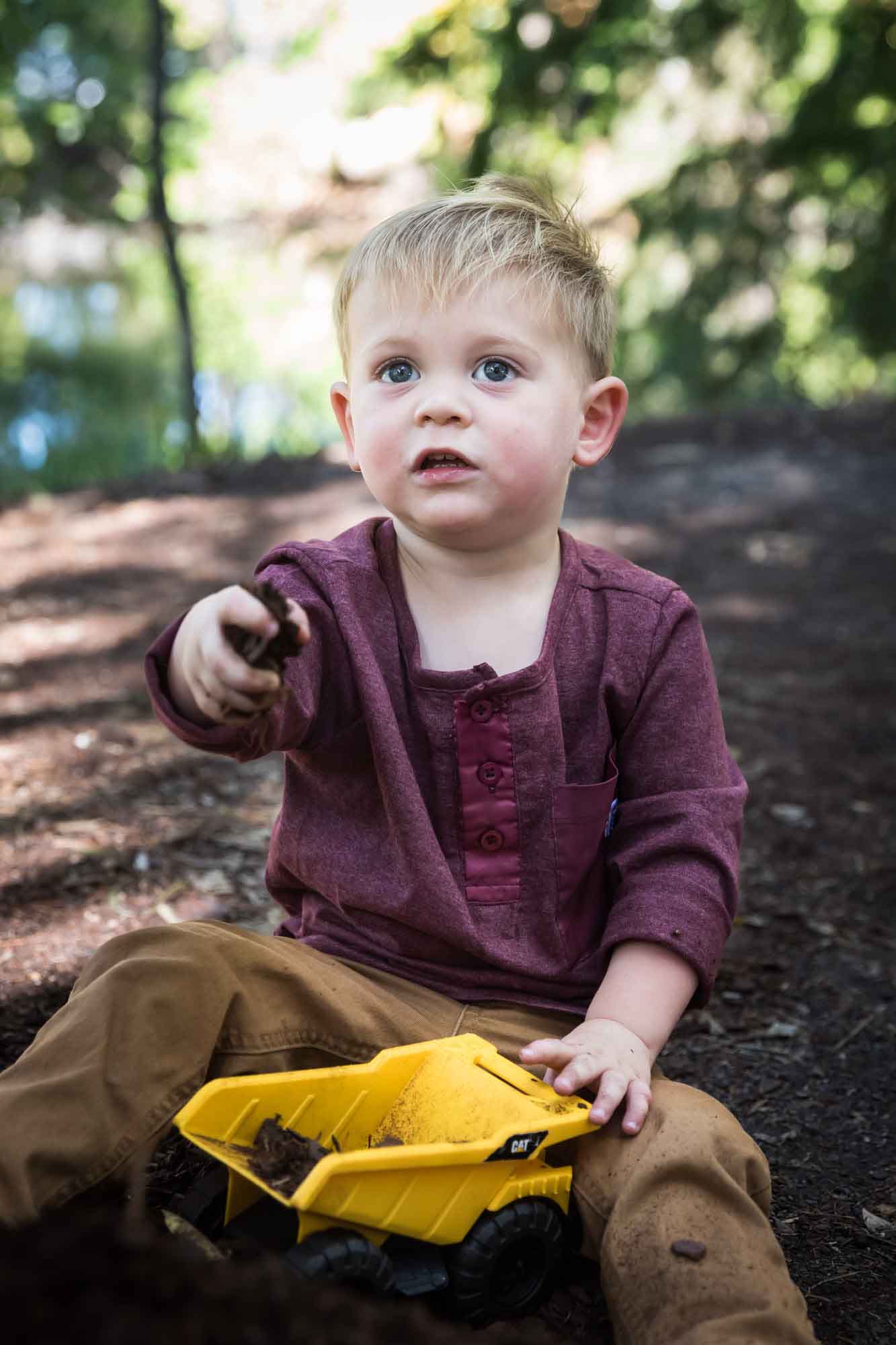 San Antonio Botanical Gardens family portrait of little boy wearing maroon shirt and khaki pants playing with mulch in his toy dump truck