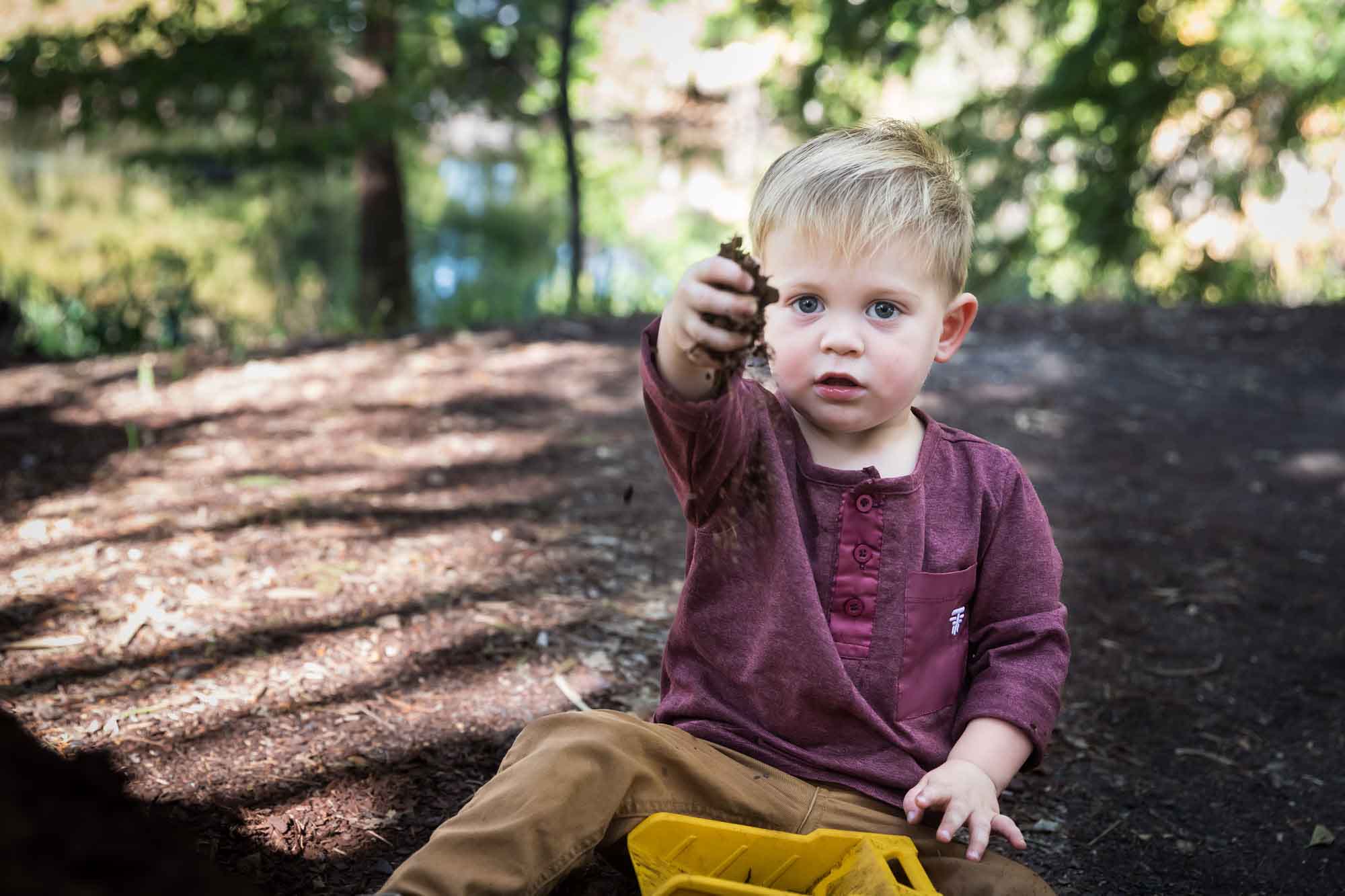 San Antonio Botanical Gardens family portrait of little boy wearing maroon shirt and khaki pants playing with mulch in his toy dump truck
