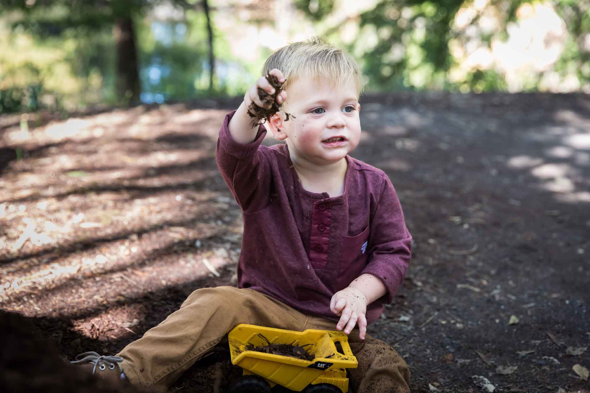 San Antonio Botanical Gardens family portrait of little boy wearing maroon shirt and khaki pants playing with mulch in his toy dump truck