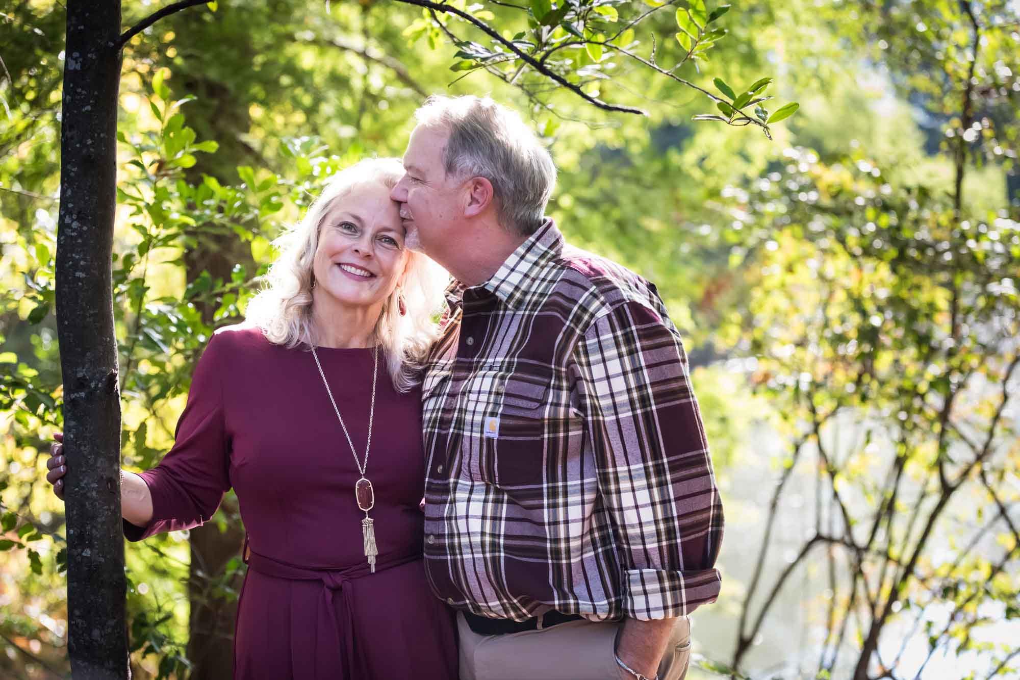 San Antonio Botanical Gardens family portrait of older man kissing older woman wearing maroon dress on the forehead in the forest