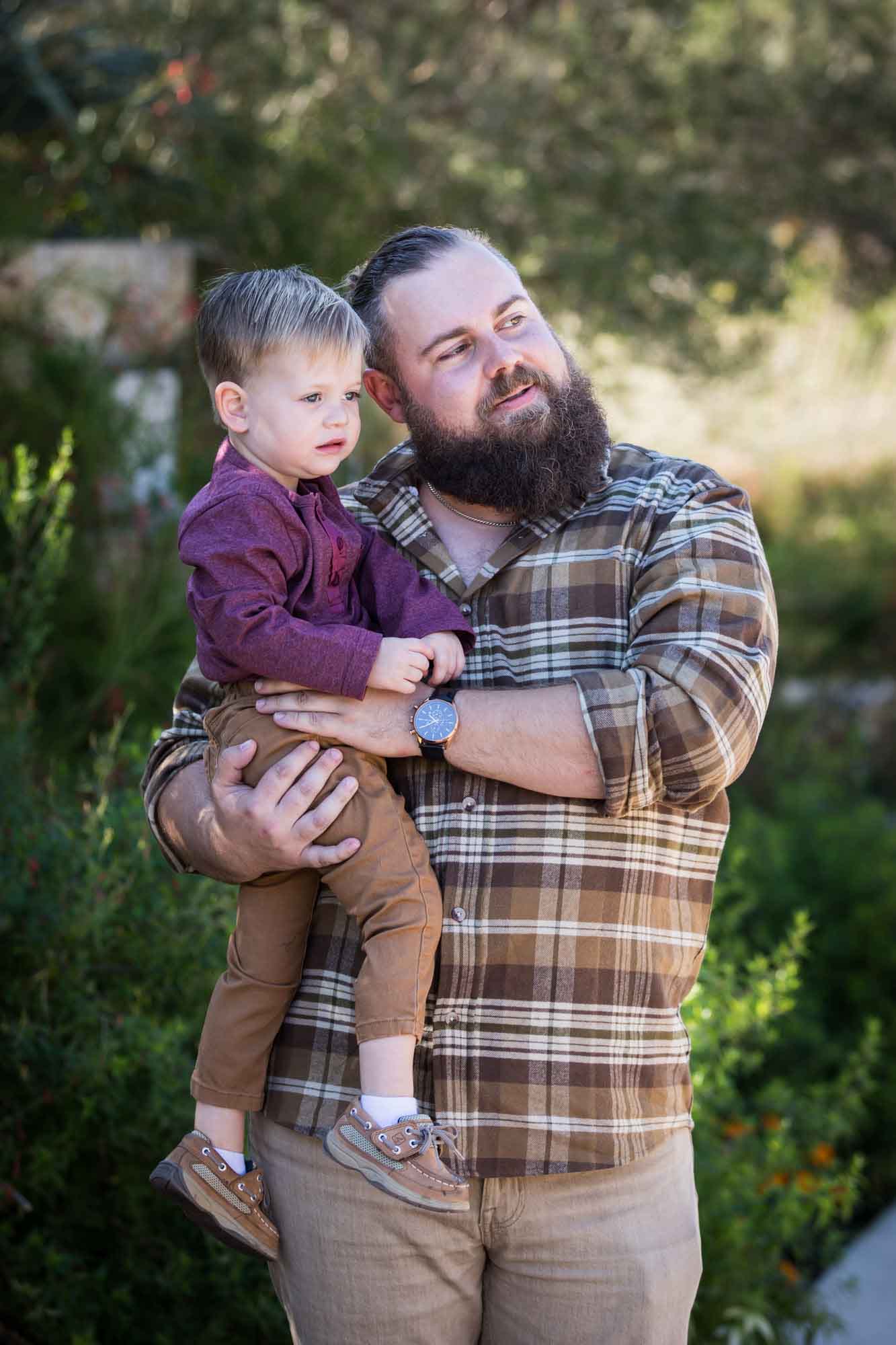 San Antonio Botanical Gardens family portrait of man wearing plaid shirt and khaki pants holding little boy wearing purple shirt and tan pants