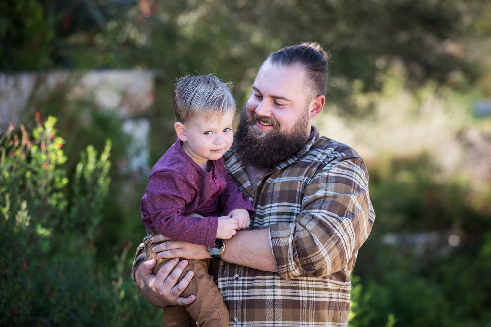 San Antonio Botanical Gardens family portrait of man wearing plaid shirt and khaki pants holding little boy wearing purple shirt and tan pants