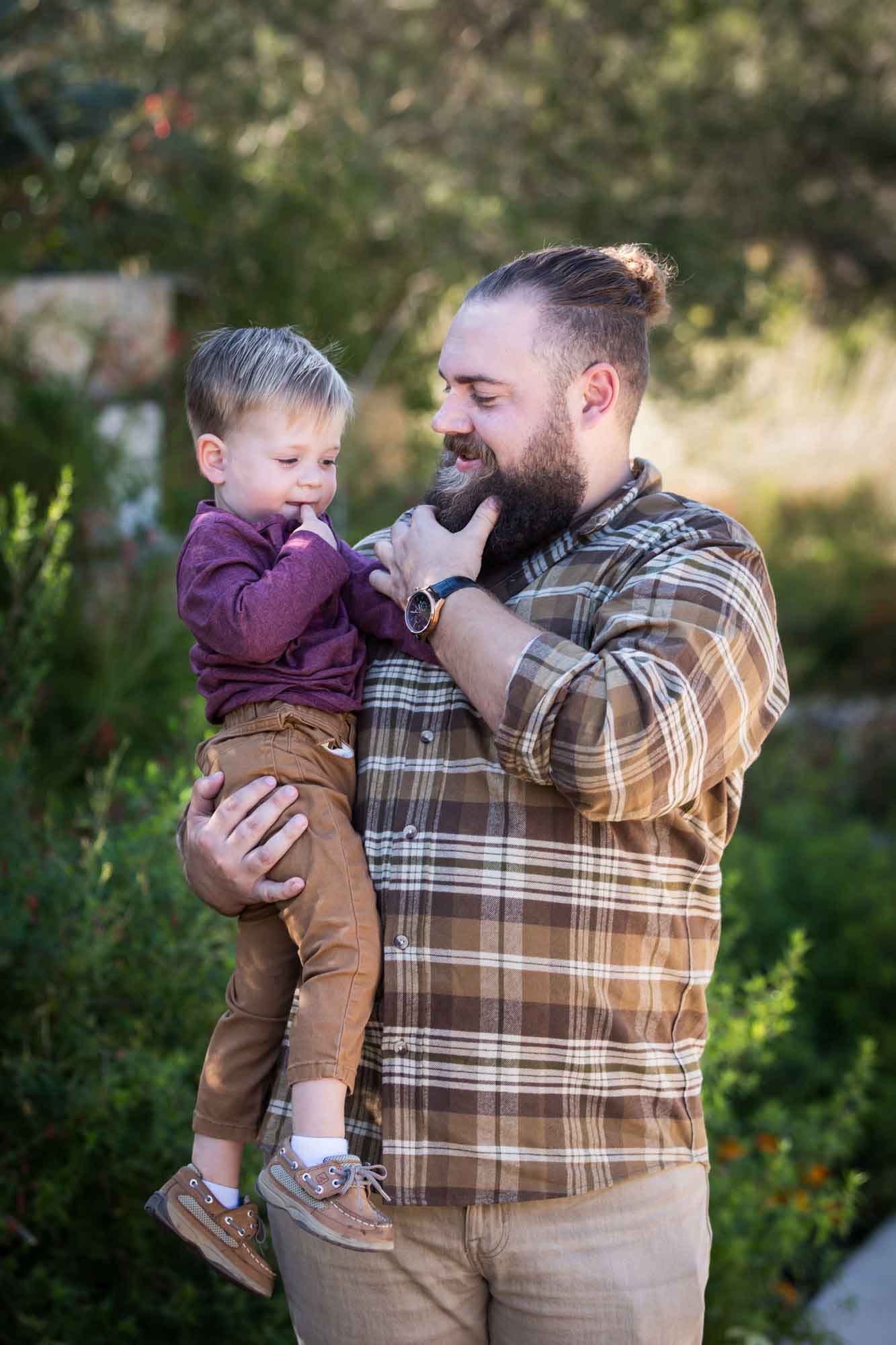 San Antonio Botanical Gardens family portrait of man wearing plaid shirt and khaki pants holding little boy wearing purple shirt and tan pants